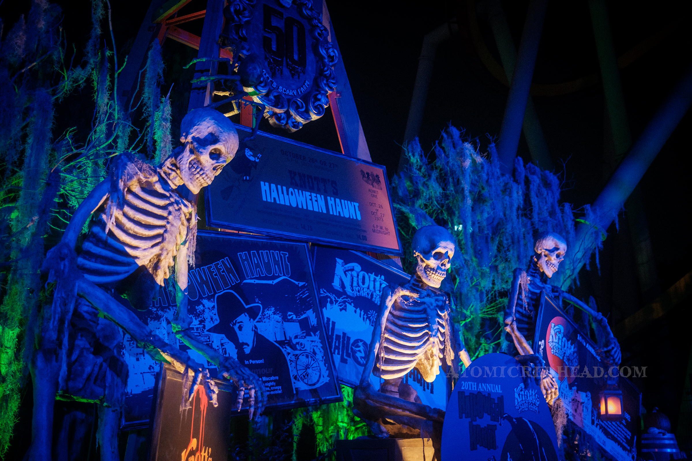 Three looming skeletons stand near various signs from past Knott's Scary Farm events.