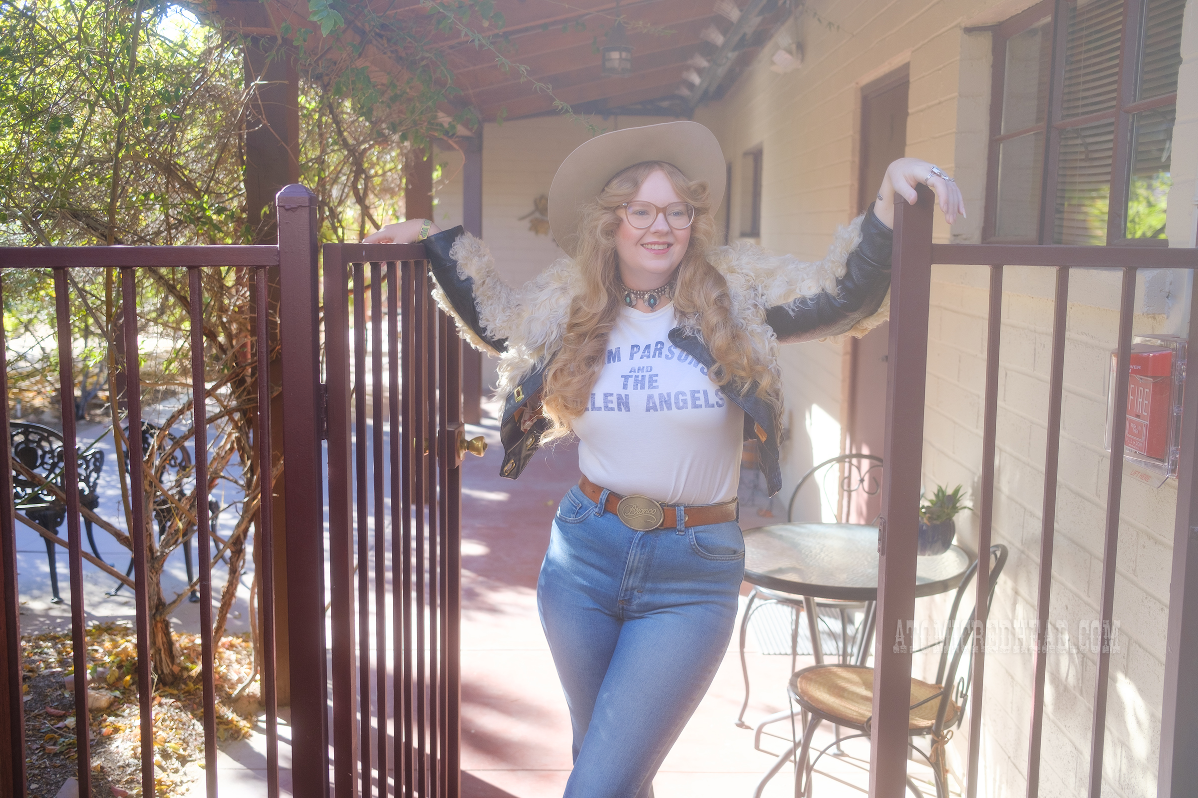 Myself, wearing a cream cowboy hat, a short jacket of cream and brown fur, a white tee reading "Gram Parsons and the Fallen Angels" in blue letters, and blue jeans.