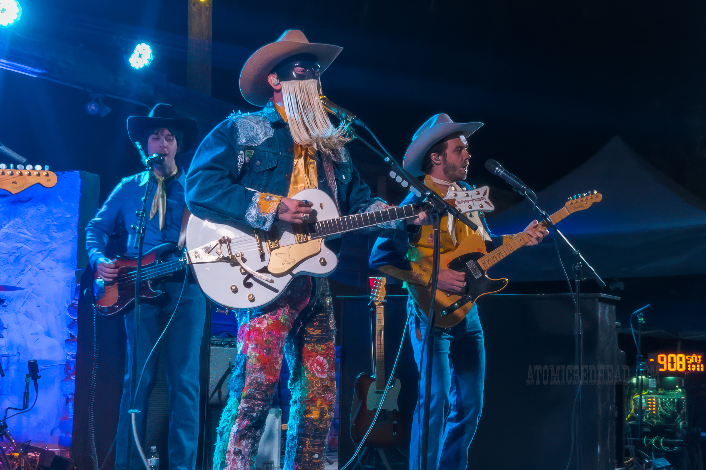 Orville Peck, wearing a jean jacket and jean pants covered in bandanas plays the guitar.