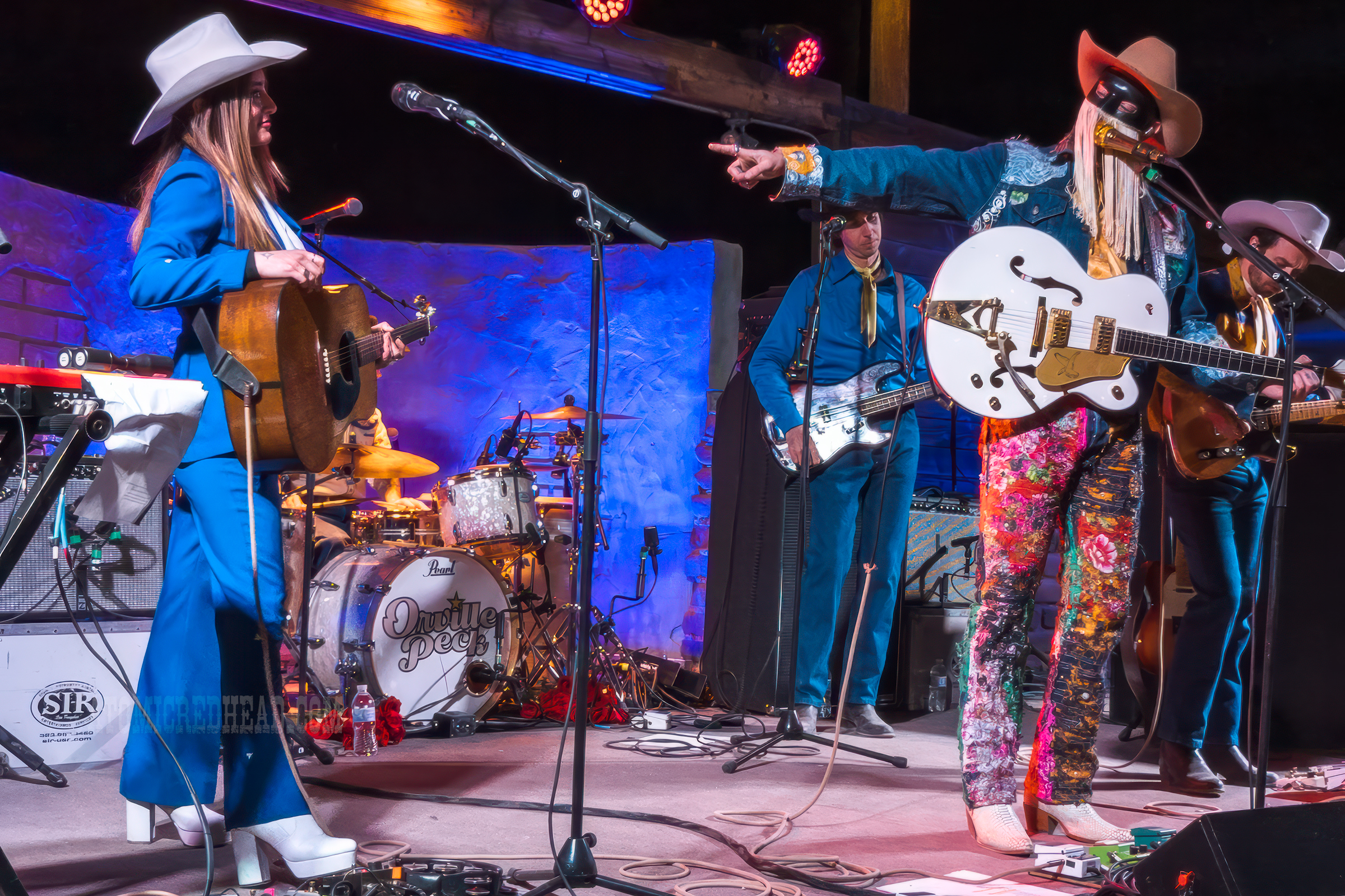 Orville Peck, wearing a jean jacket and jean pants covered in bandanas plays the guitar