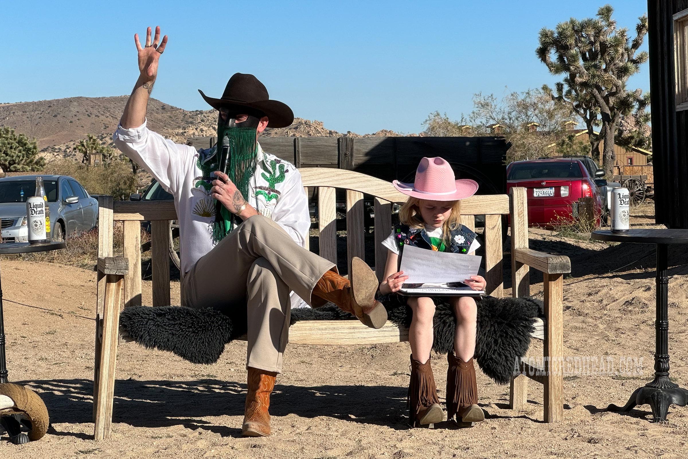 Orville, wearing a white shirt with sequin cacti on it, tan pants, and black cowboy hat sits on a bench with his seven year old niece.