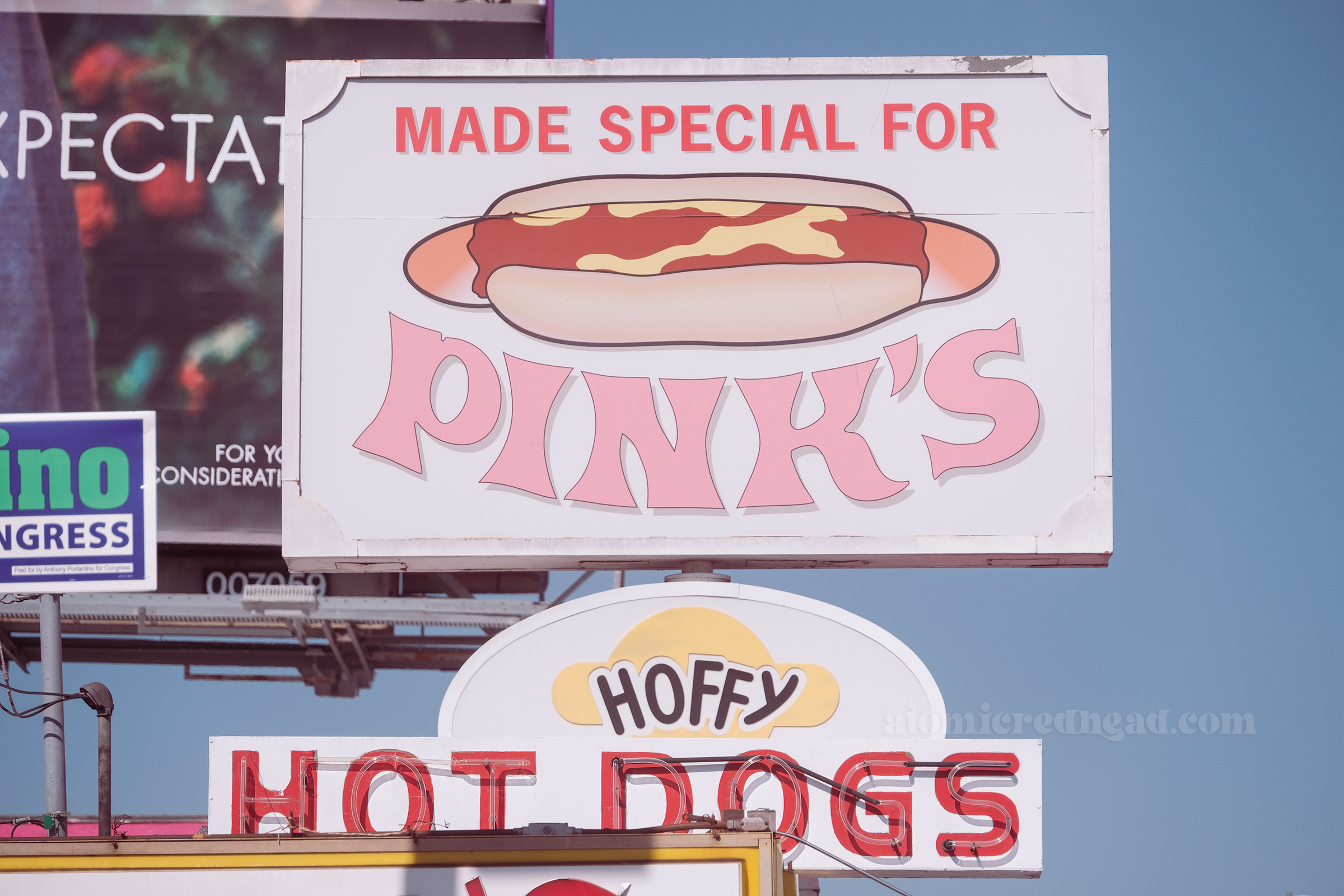 Close-up of the backlit plastic sign on the roof that features a large hot dog and reads "Made Special for Pinls" and below another sign reading "Hoffy" in front is a small neon sign reading "Hot Dogs"