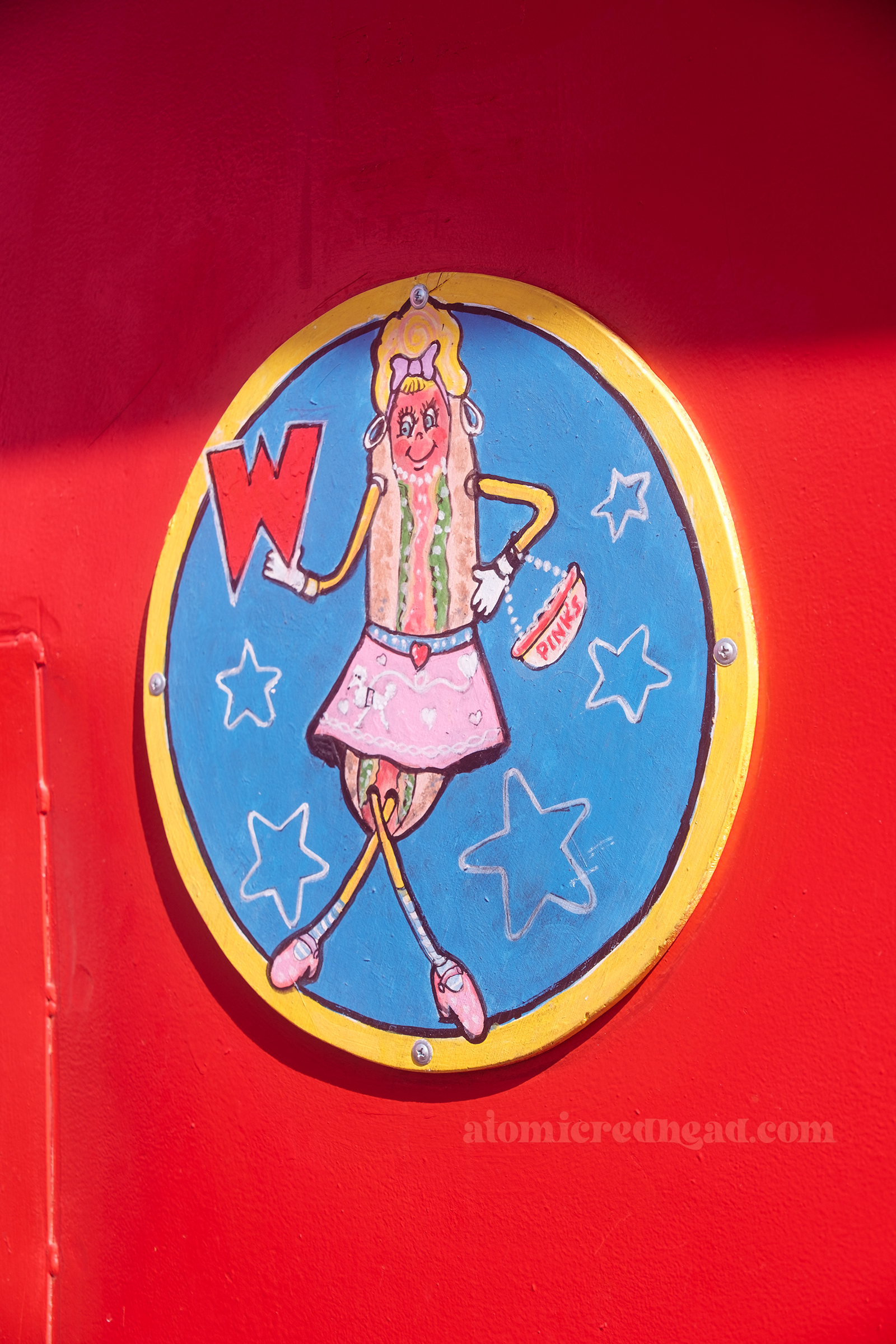 Sign for the women's restroom features a hot dog in a pink dress and blonde hair holding a large red letter "W"