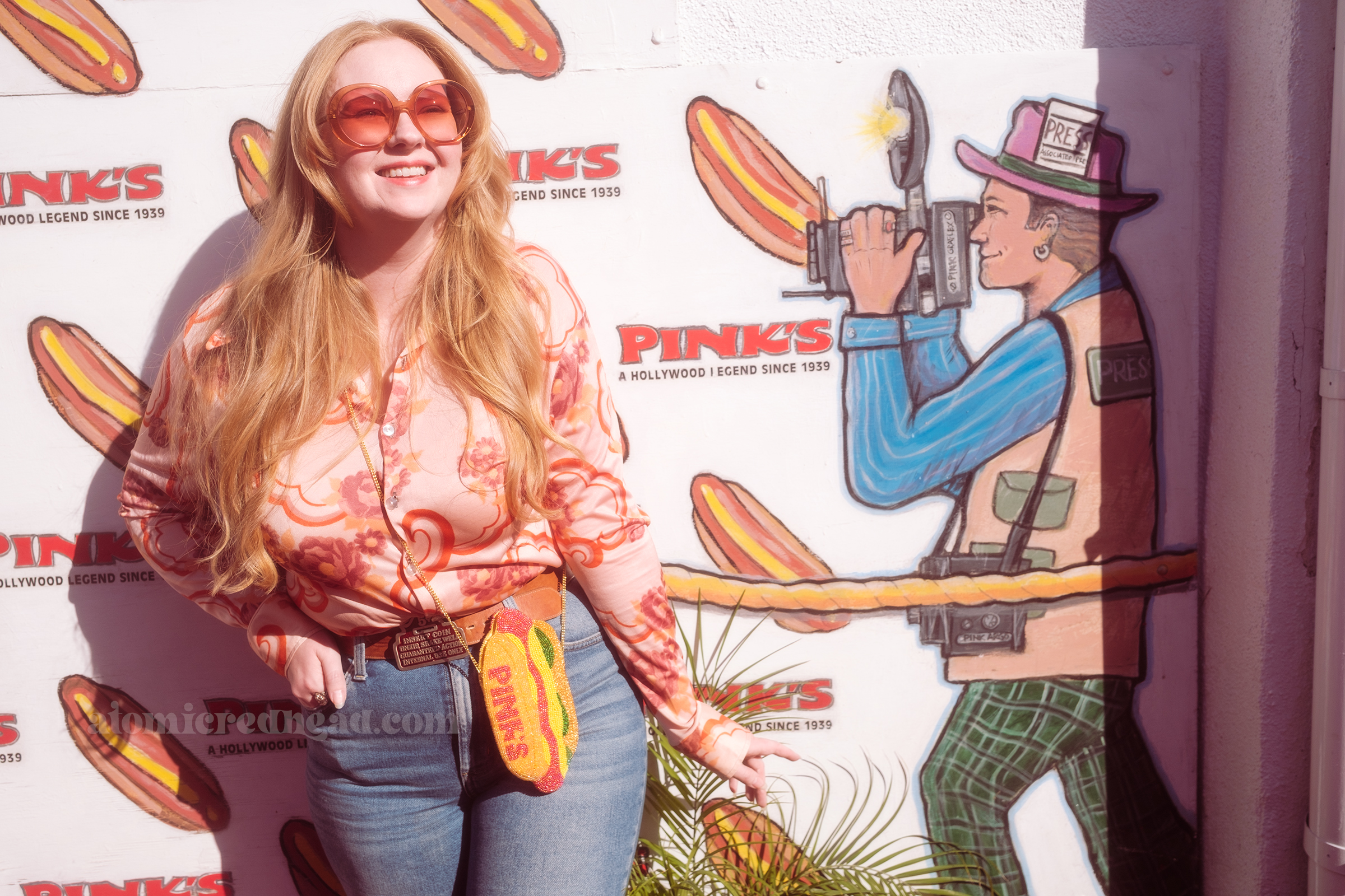 Myself, wearing a pink shirt with a psychedelic pattern in front of a wall with a mural of photographers. 