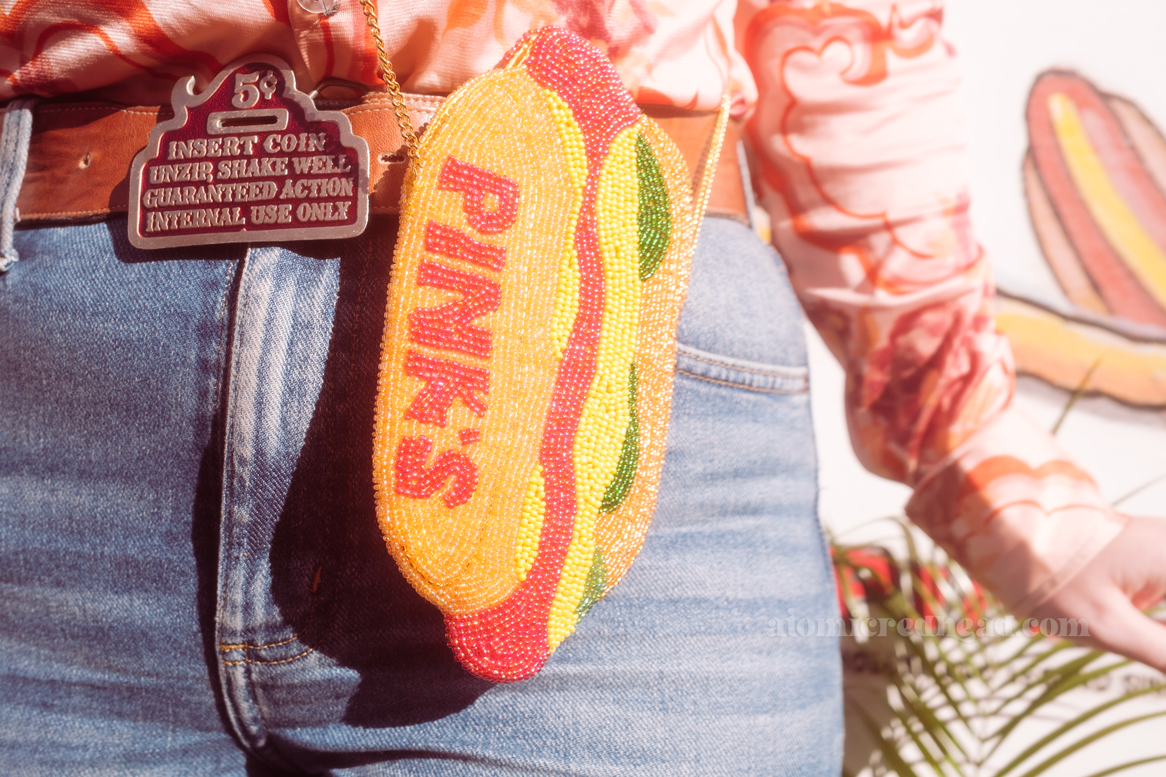 Close-up of a beaded purse of a hot dog that reads "Pink's" and my belt buckle that reads "5 cents Insert Coin Unzip Shake Well Guaranteed Action Internal Use Only"