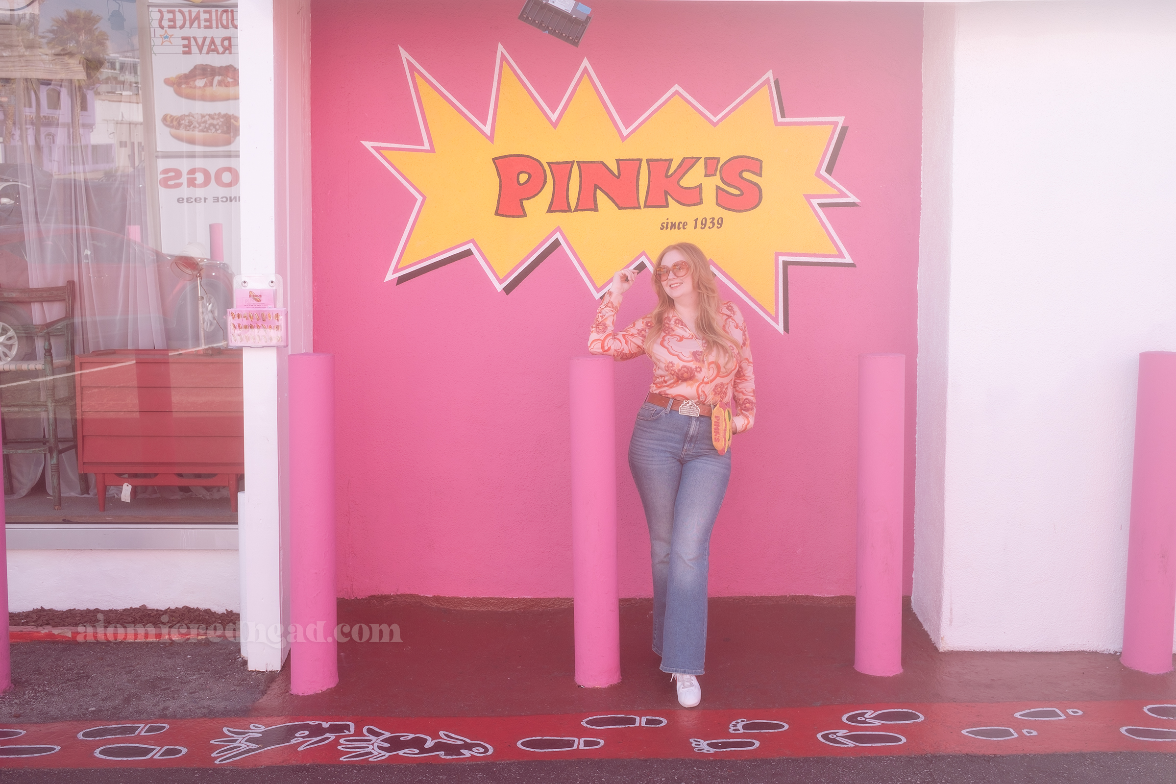 Myself standing in front of a large pink wall that features a burst of yellow and inside it reads "Pink's Since 1939" in red letters.