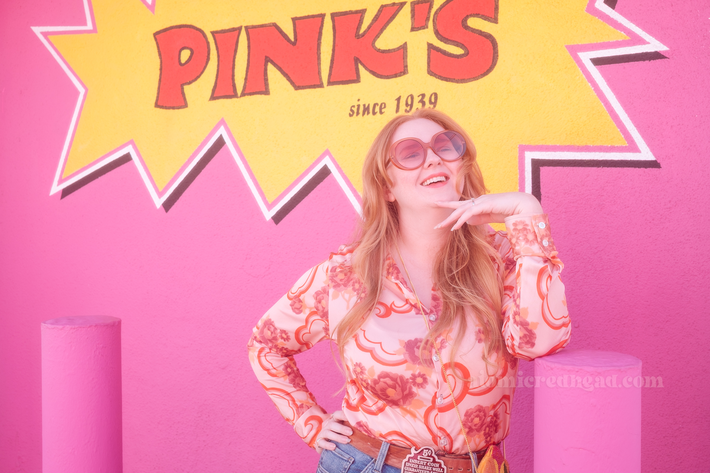 Myself standing in front of a large pink wall that features a burst of yellow and inside it reads "Pink's Since 1939" in red letters.