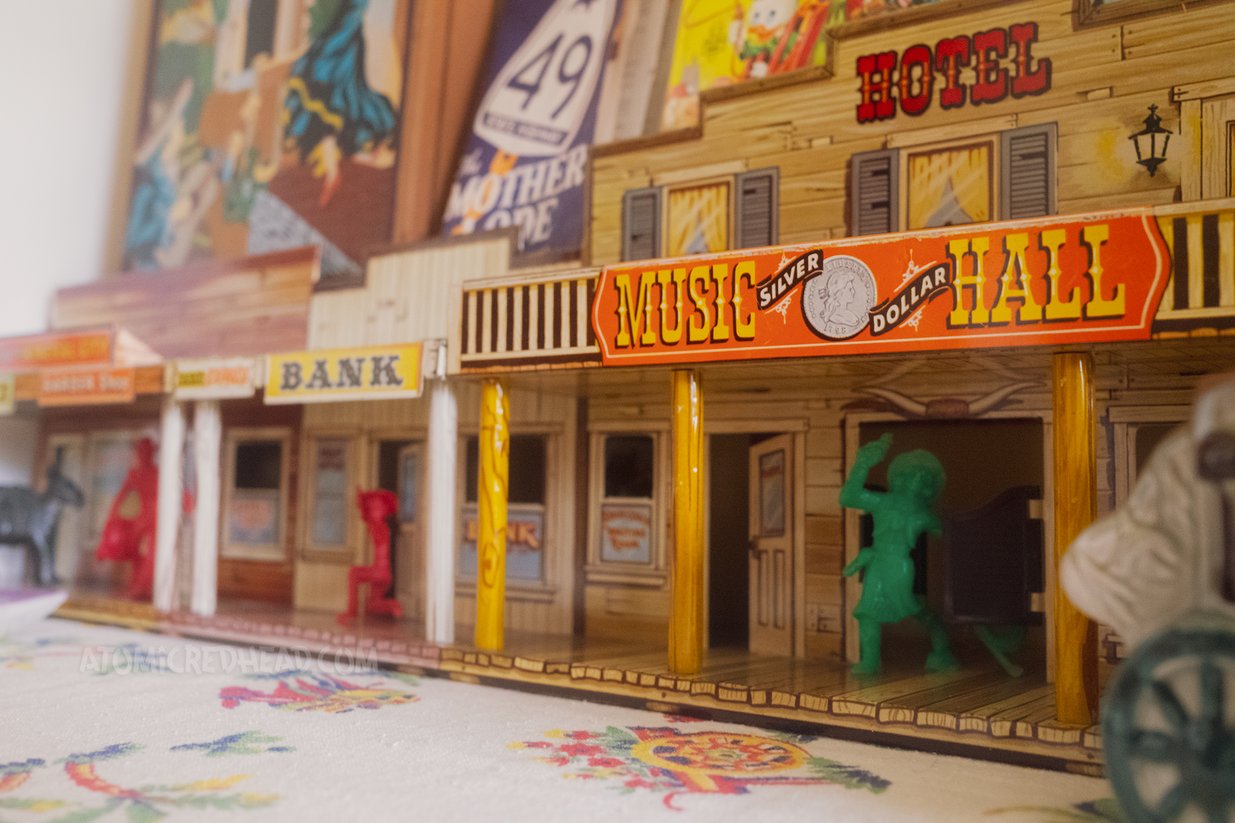 Close-up of the tin western town, featuring small toy cowgirl and cowboys coming from doorways.