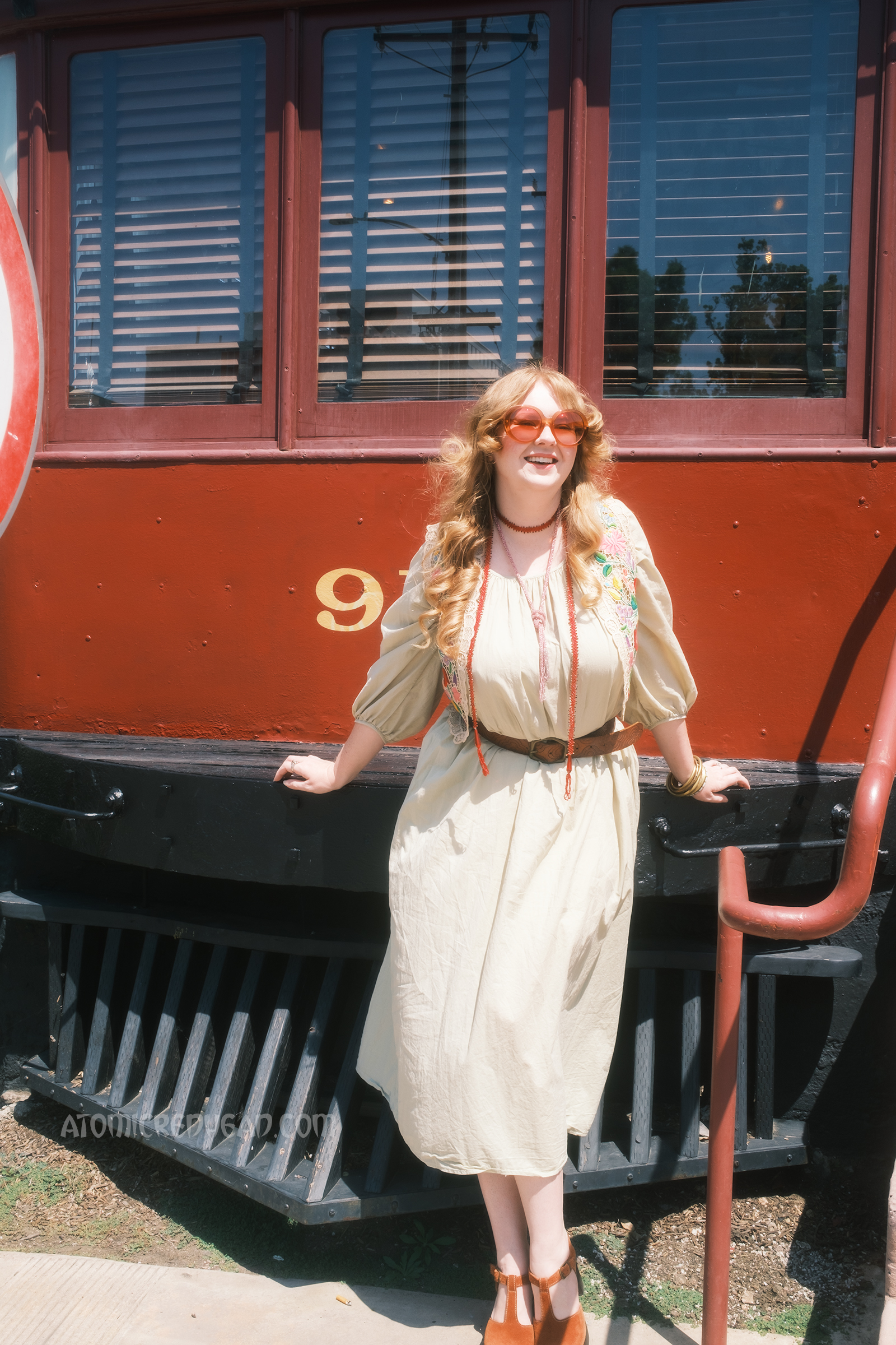 Myself, wearing a pale green dress with an embroidered lace vest featuring a floral design, standing in front of the train car.