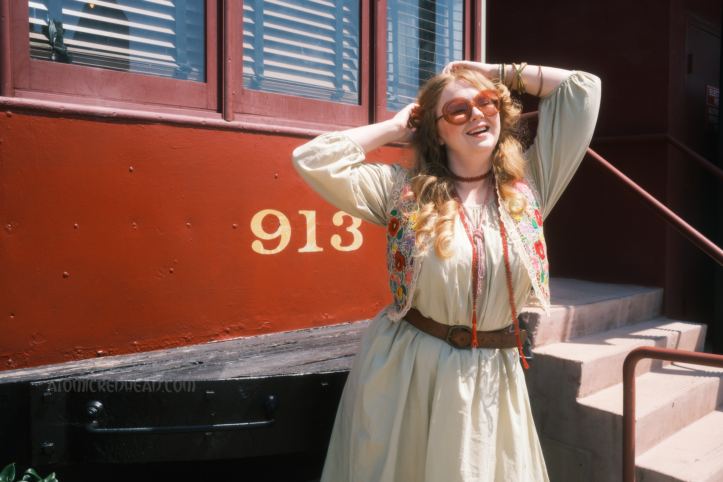 Myself, wearing a pale green dress with an embroidered lace vest featuring a floral design, standing in front of the train car.