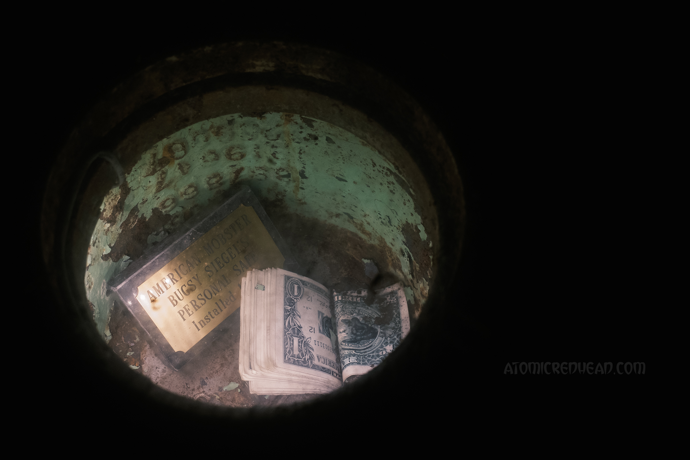 Close-up of a circular window in the floor, several bills are folded inside and there is a small gold plaque reading "American Mobster Bugsy Siegel's Personal Safe"