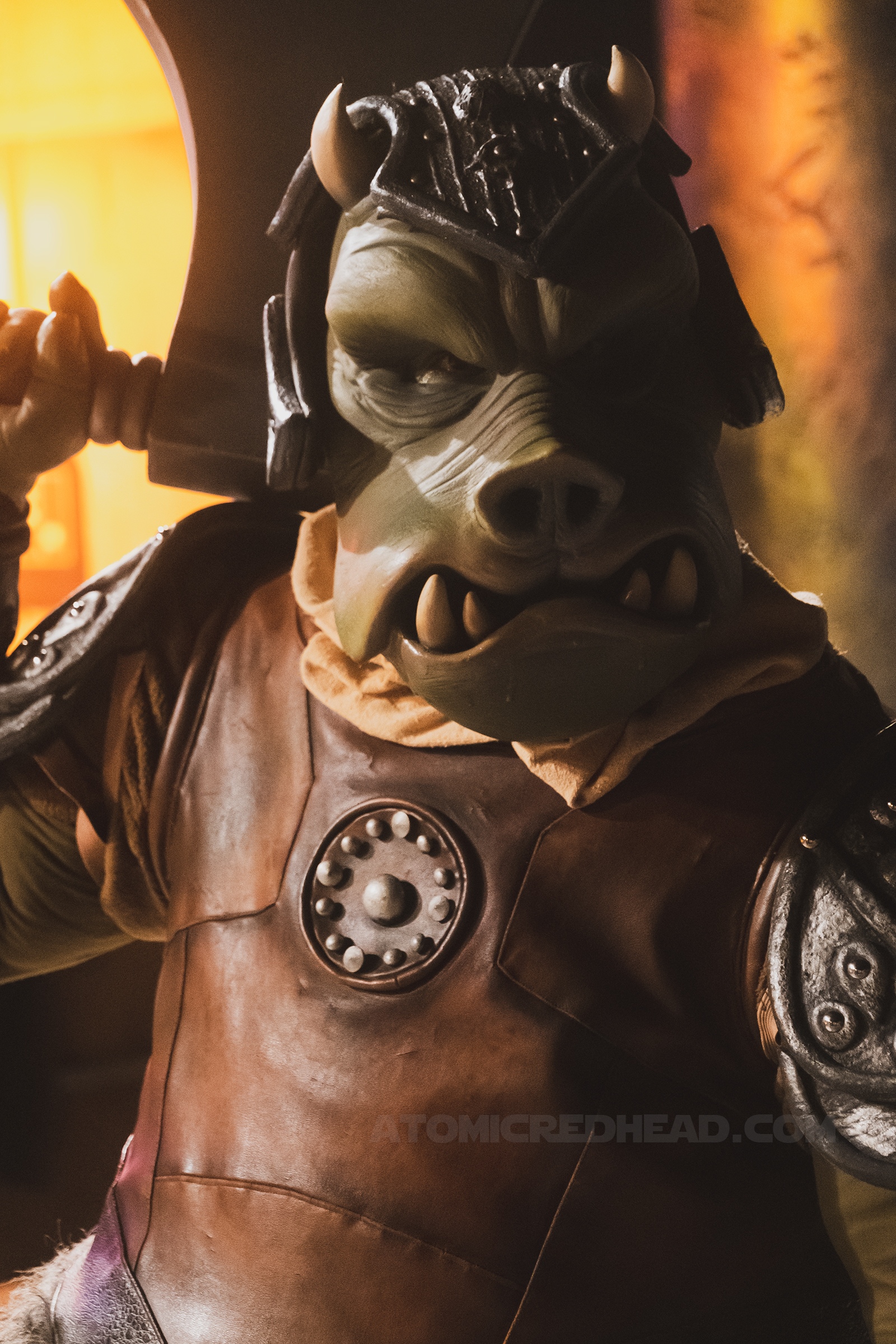 Jaba's gamorrean guard, a green pig like creature in brown attire glares at those approaching Jaba.