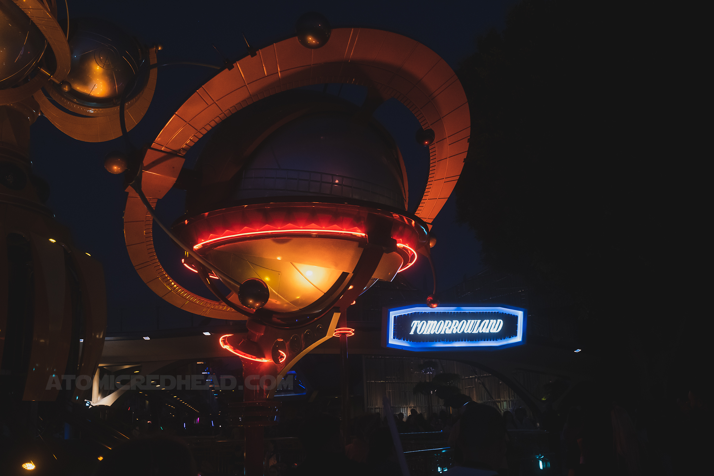 View of Tomorrowland, a copper orb, part of the Rocket Jets attraction is on the left, to the right is a white and blue lighted sign that reads "Tomorrowland"