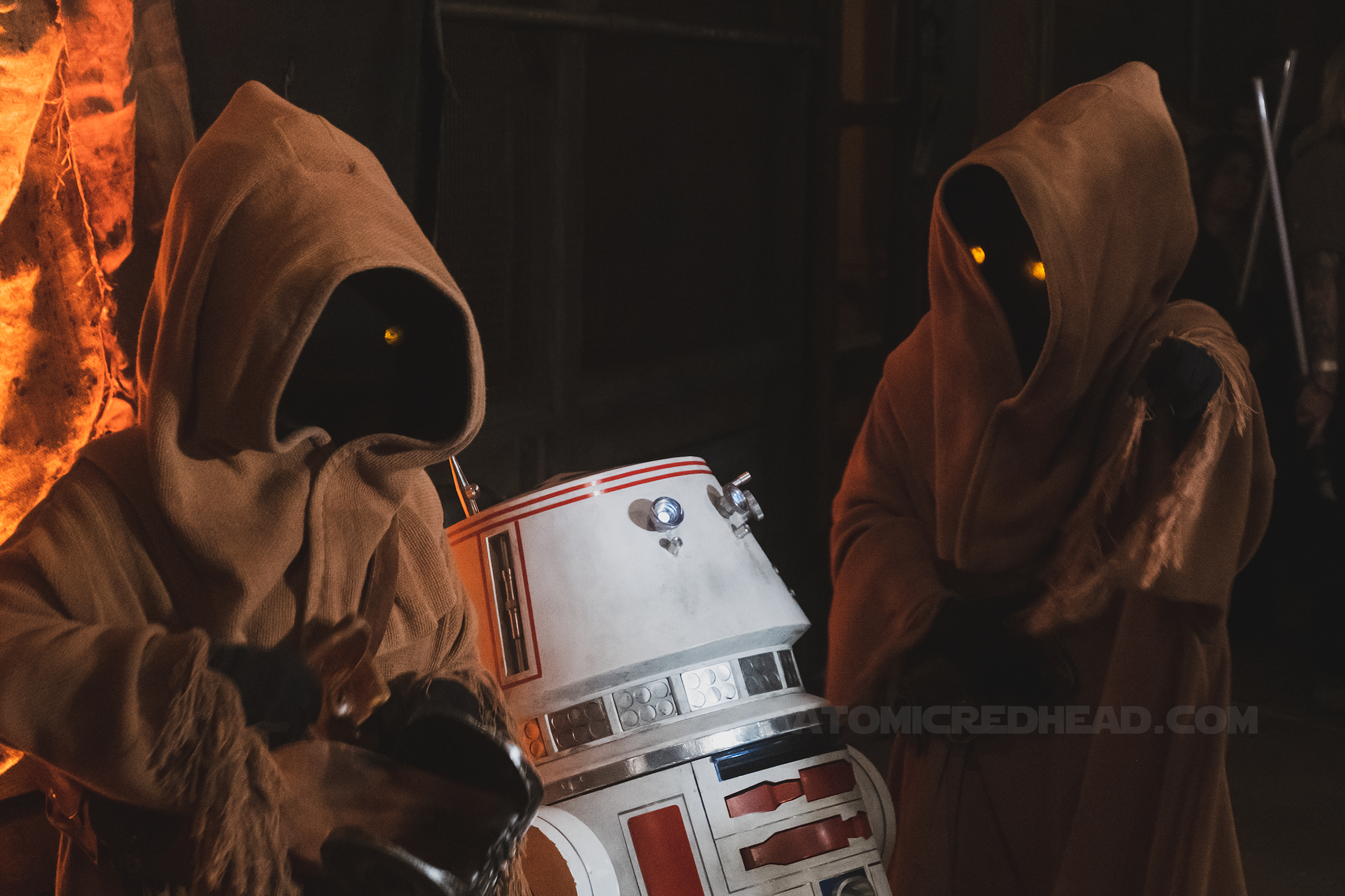 Jawas, creatures wearing brown robes and covered faces interact with R5, a red and white droid.