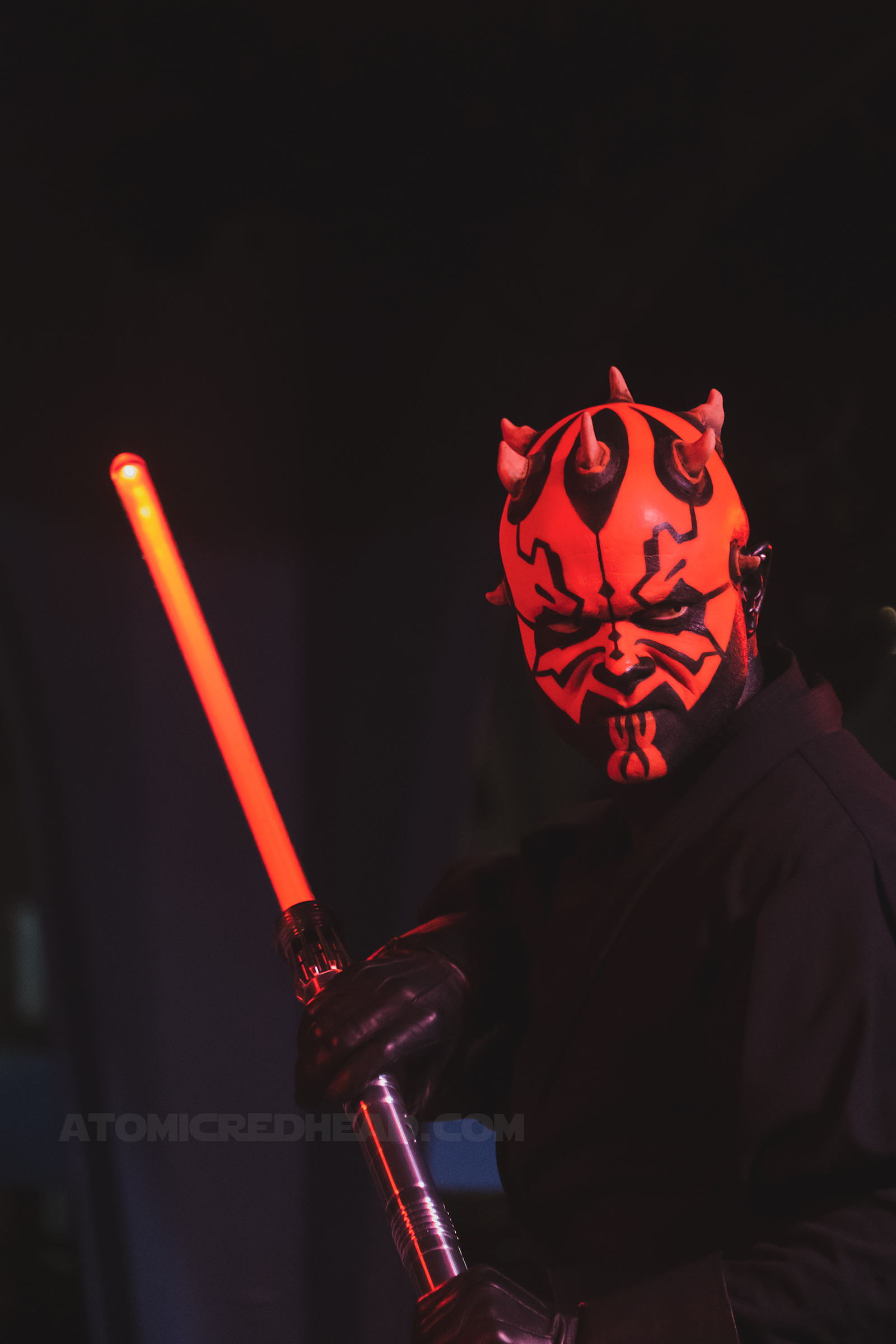 Darth Maul, featuring a face of red and black with horns on his head wields a red lightsaber.