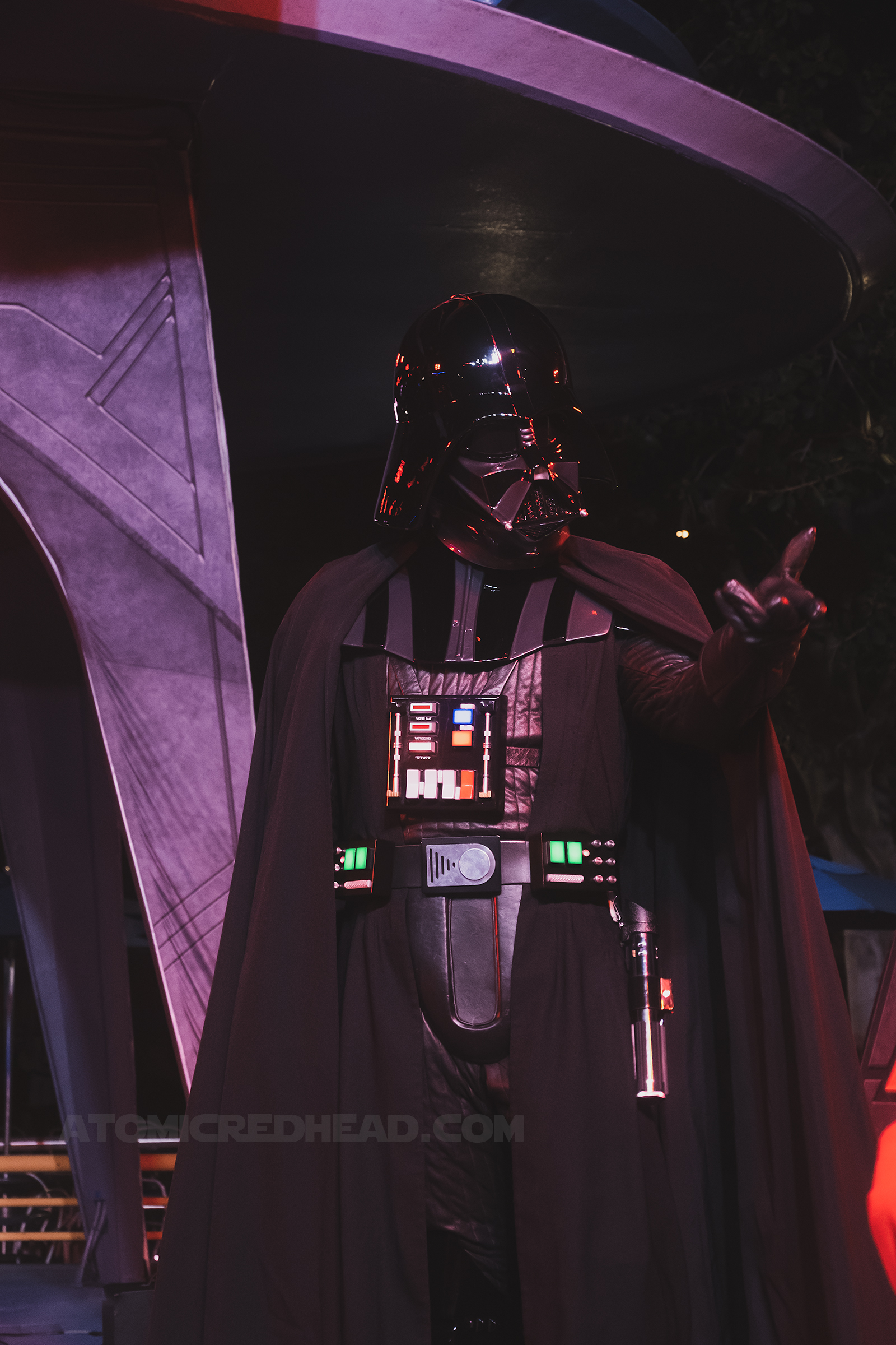 Darth Vader, clad in all black and a helmet reaches towards Guests.