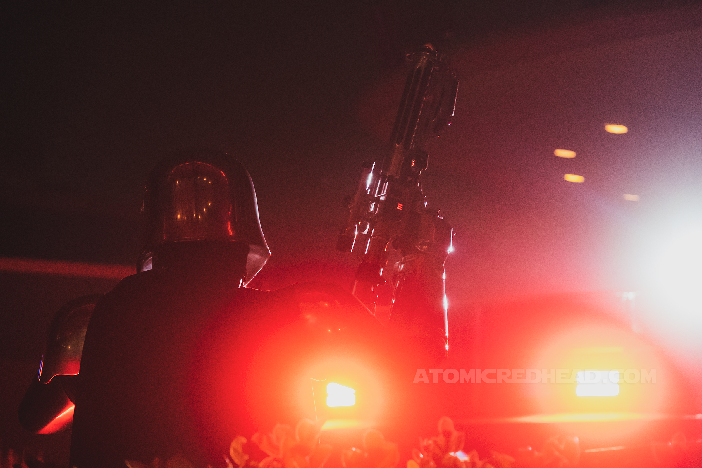 Captain Phasma raises her blaster into the air and is lit with red light from behind.