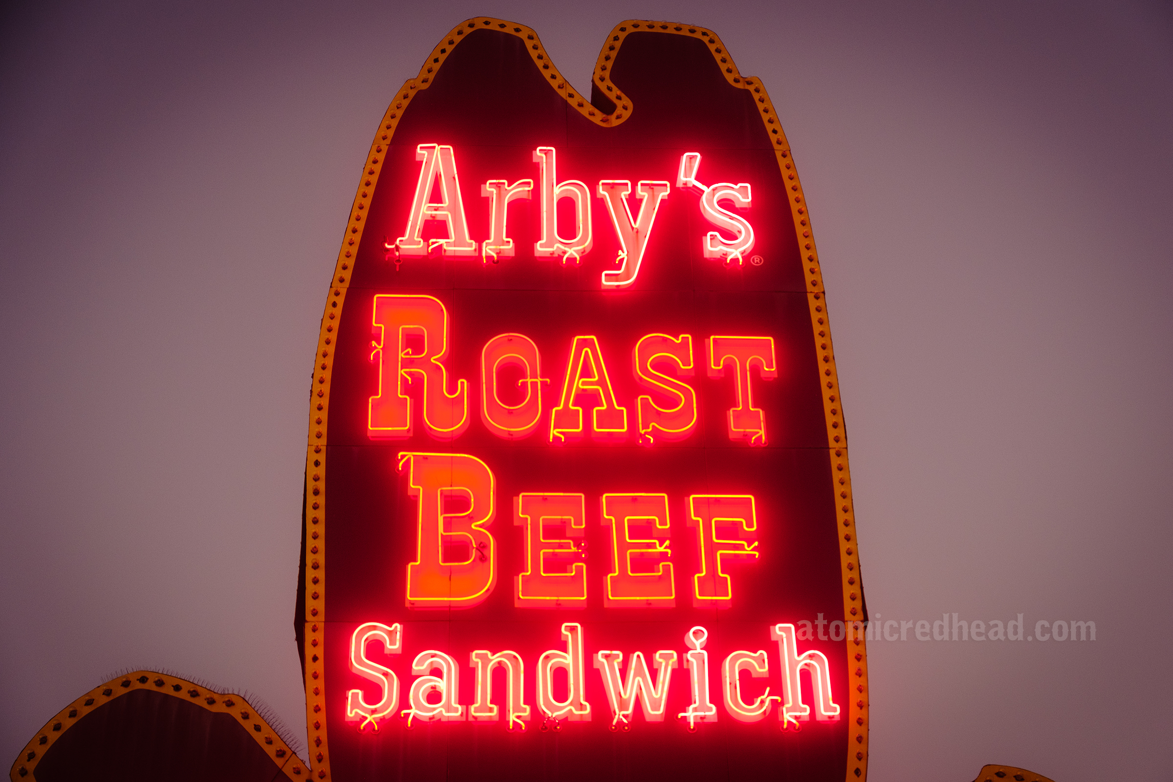 Close-up of the sign lit up at night reading "Arby's Roast Beef Sandwich"