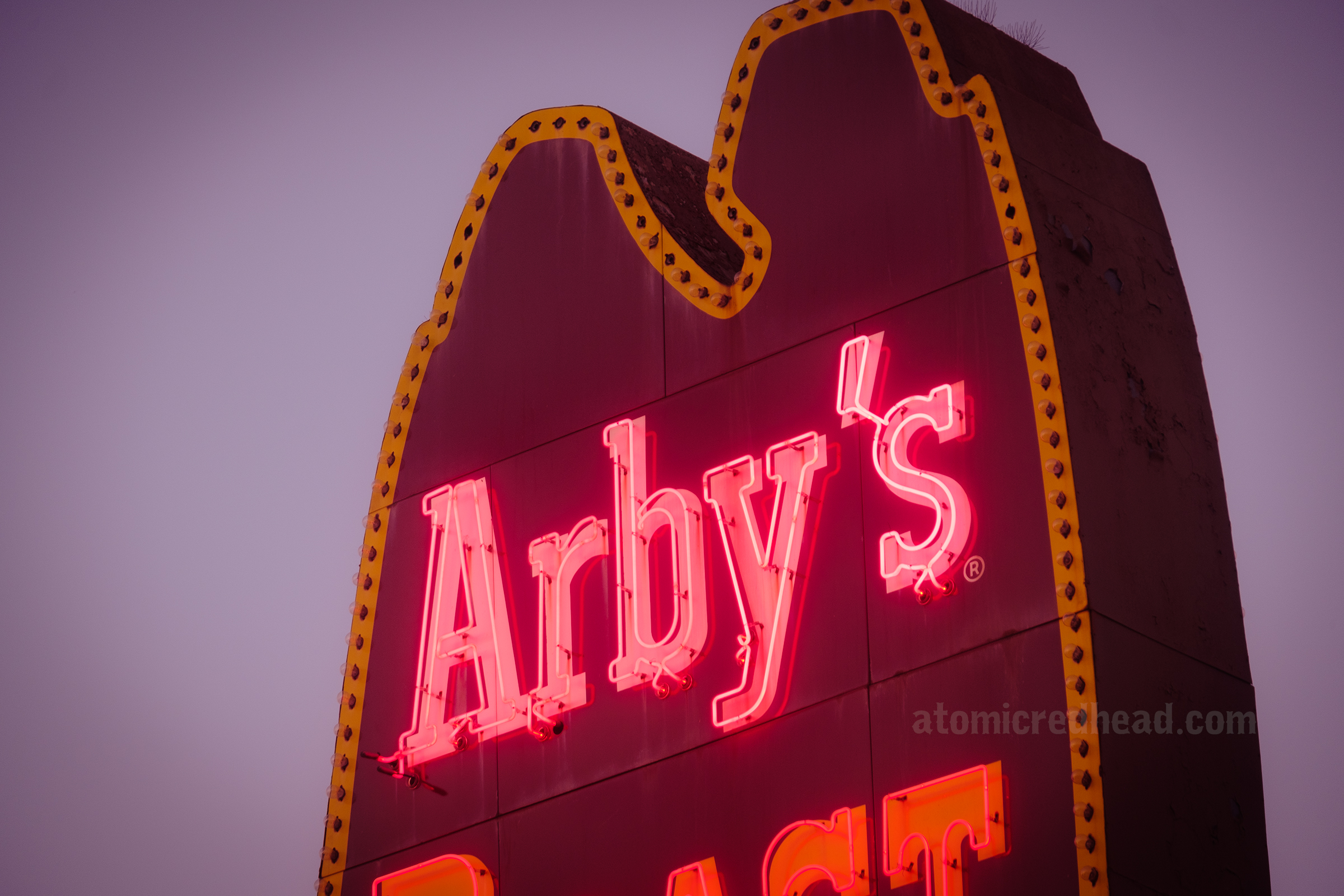 Close-up of the "Arby's" portion of the neon sign lit up at night.