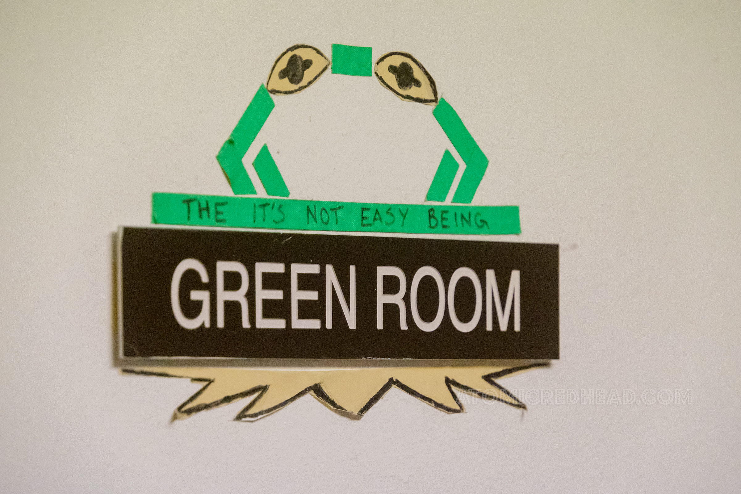 A black and whit sign reading "Green Room" has been modified with tape and stickers to look like Kermit the frog, and now reads The It's Not Easy Being Green Room"