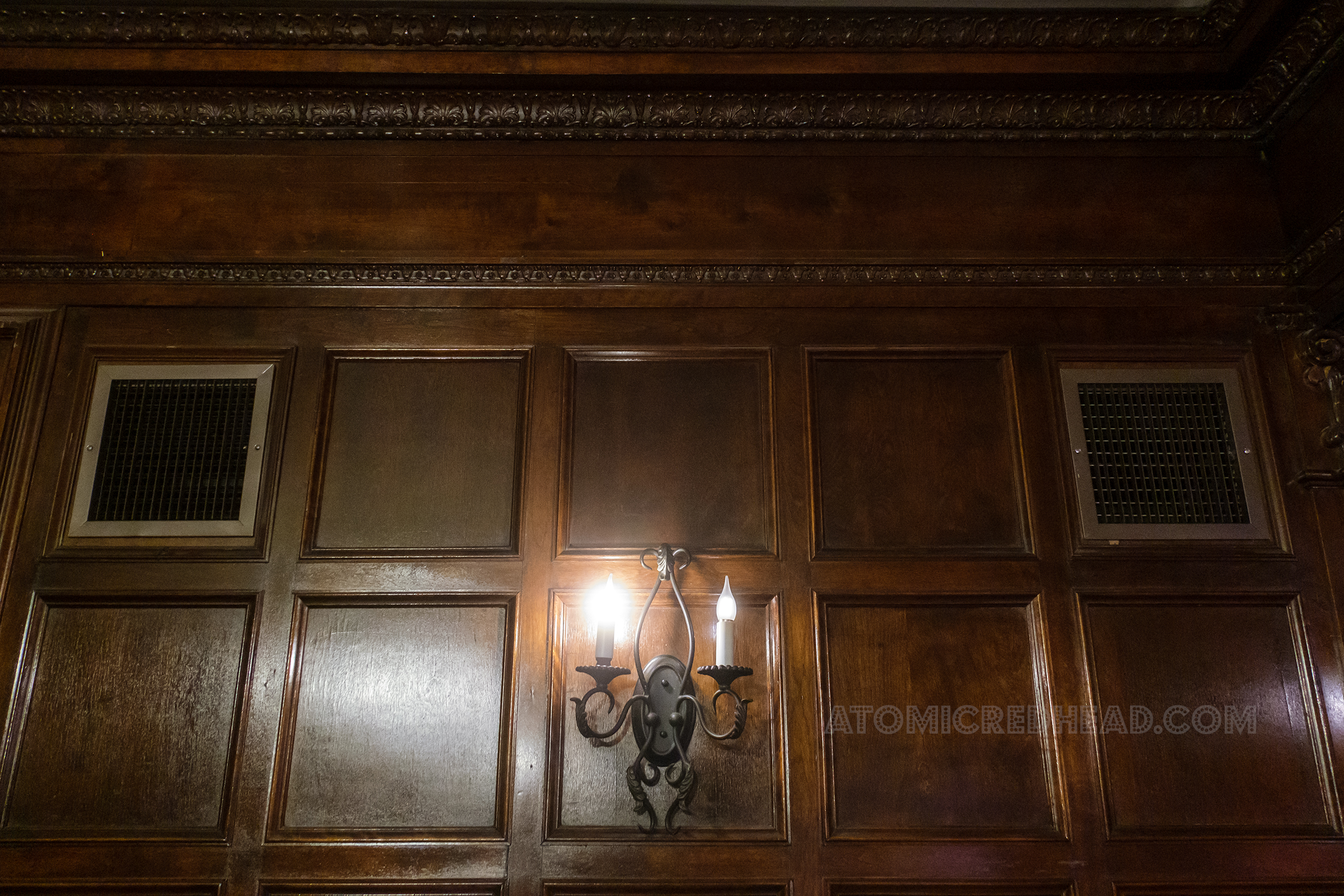 A sconce featuring faux candles hangs on a rich wood paneled wall.