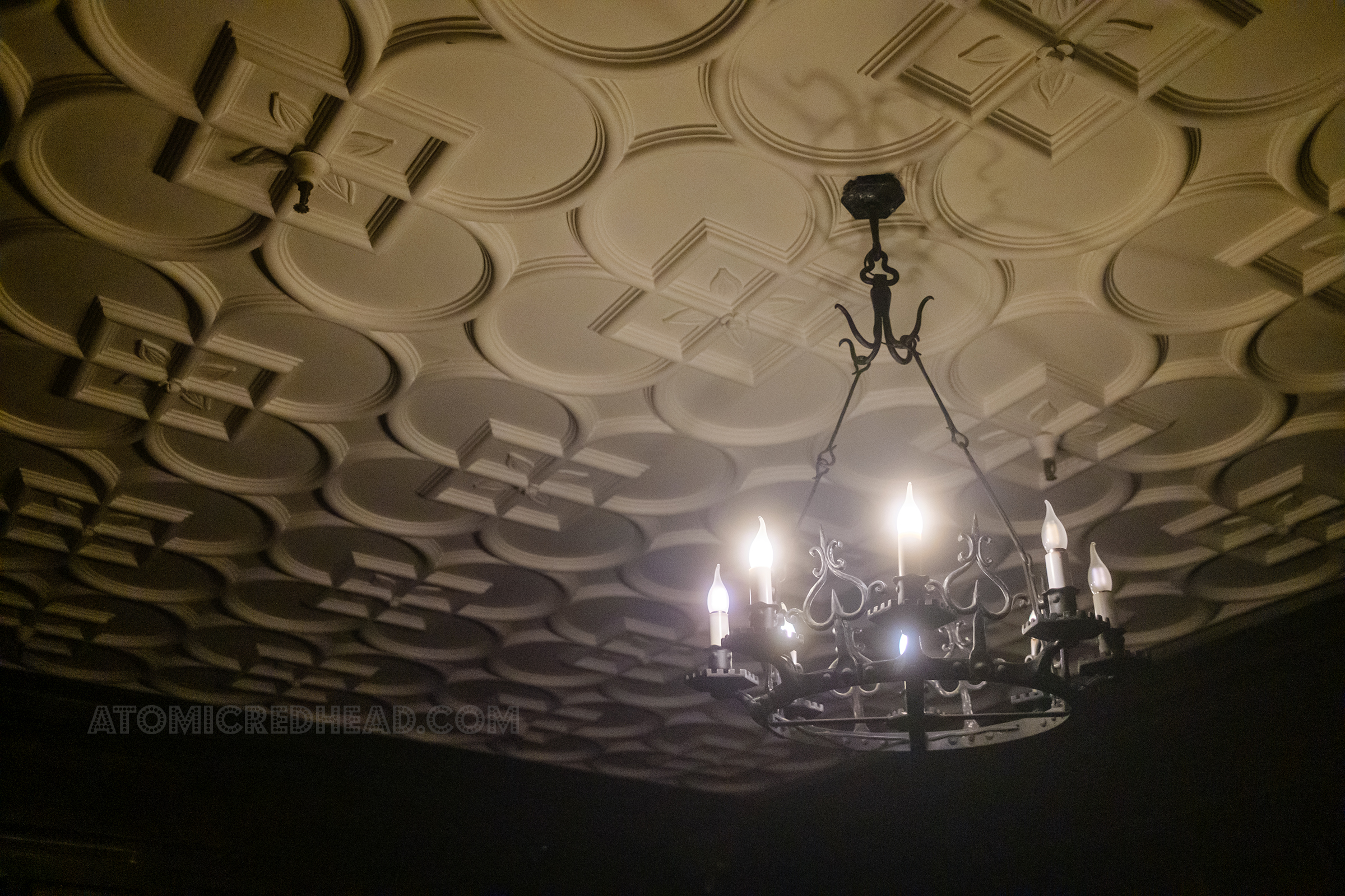 A wrought iron chandelier with faux candles hangs from a white ceailing.