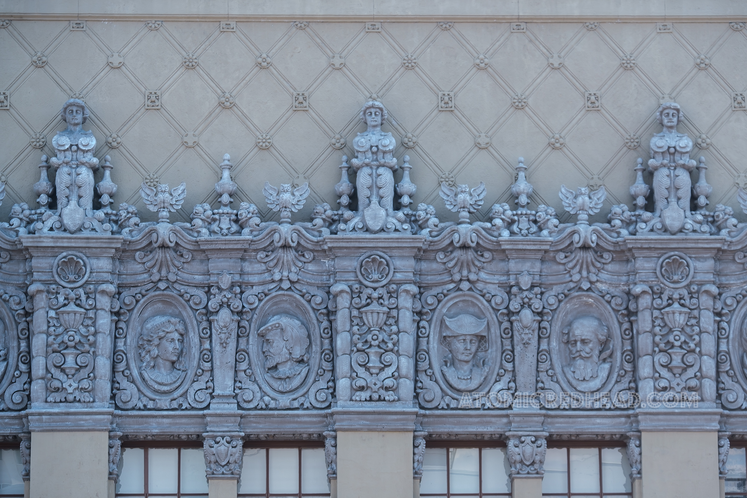 Close-up of the detailed relief work, that includes birds, male and female faces, and floral embellishments. 