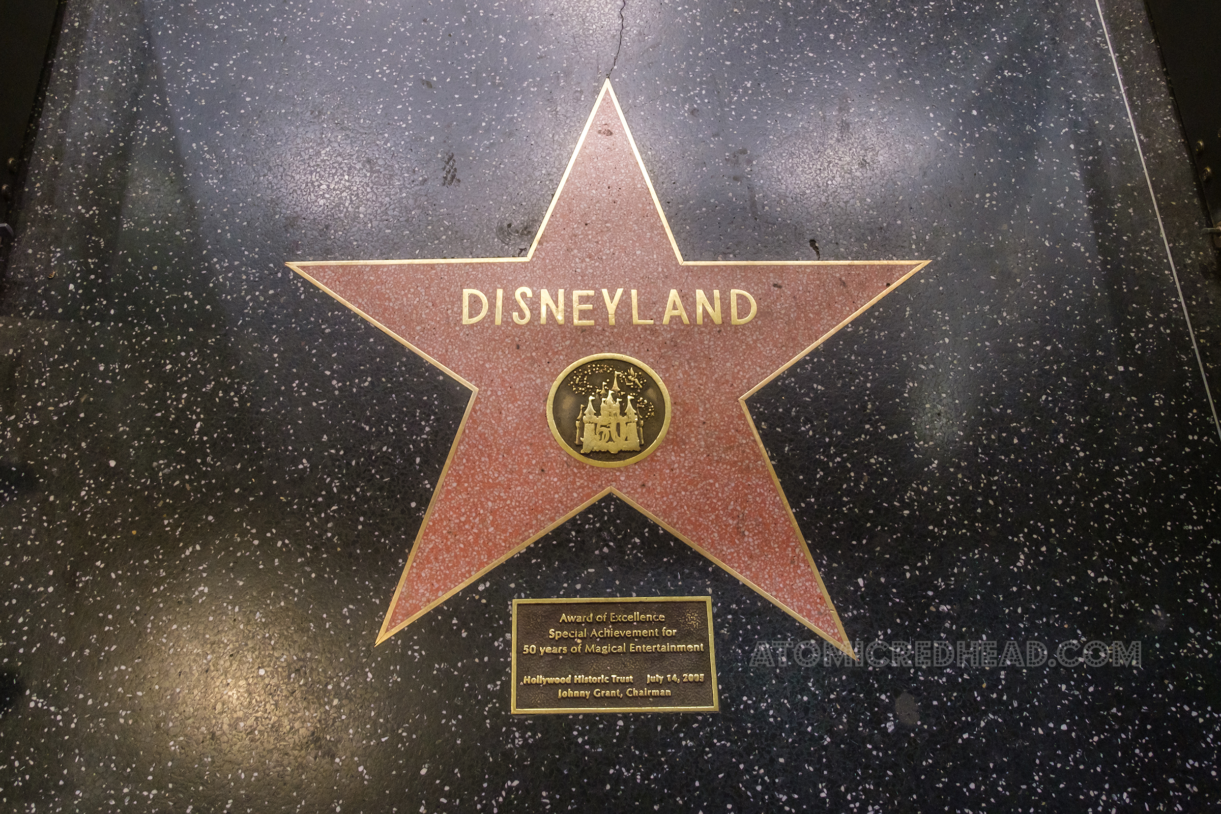 Along the Hollywood Walk of Fame sits the pink star reading "Disneyland" in gold letters and features a small gold castle. Below a small plaque reads "Aware of Excellence Special Achievement for 50 years of Magical Entertainment Hollywood Trust July 14 2005 Johnny Grant, Chairman"