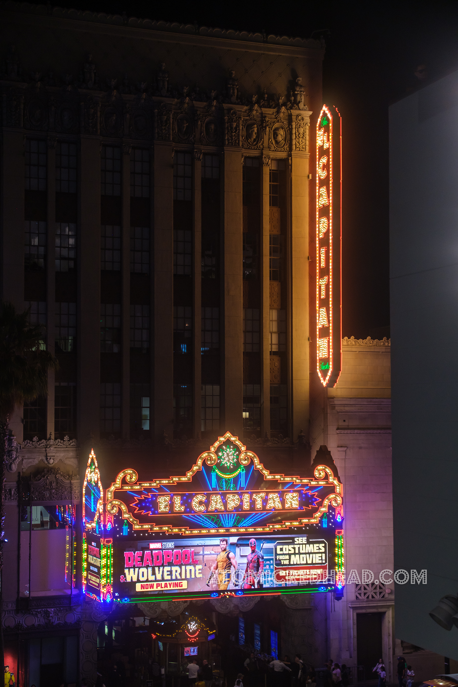 Overall of the El Capitan exterior lit up at night with colorful neon and bulbs.