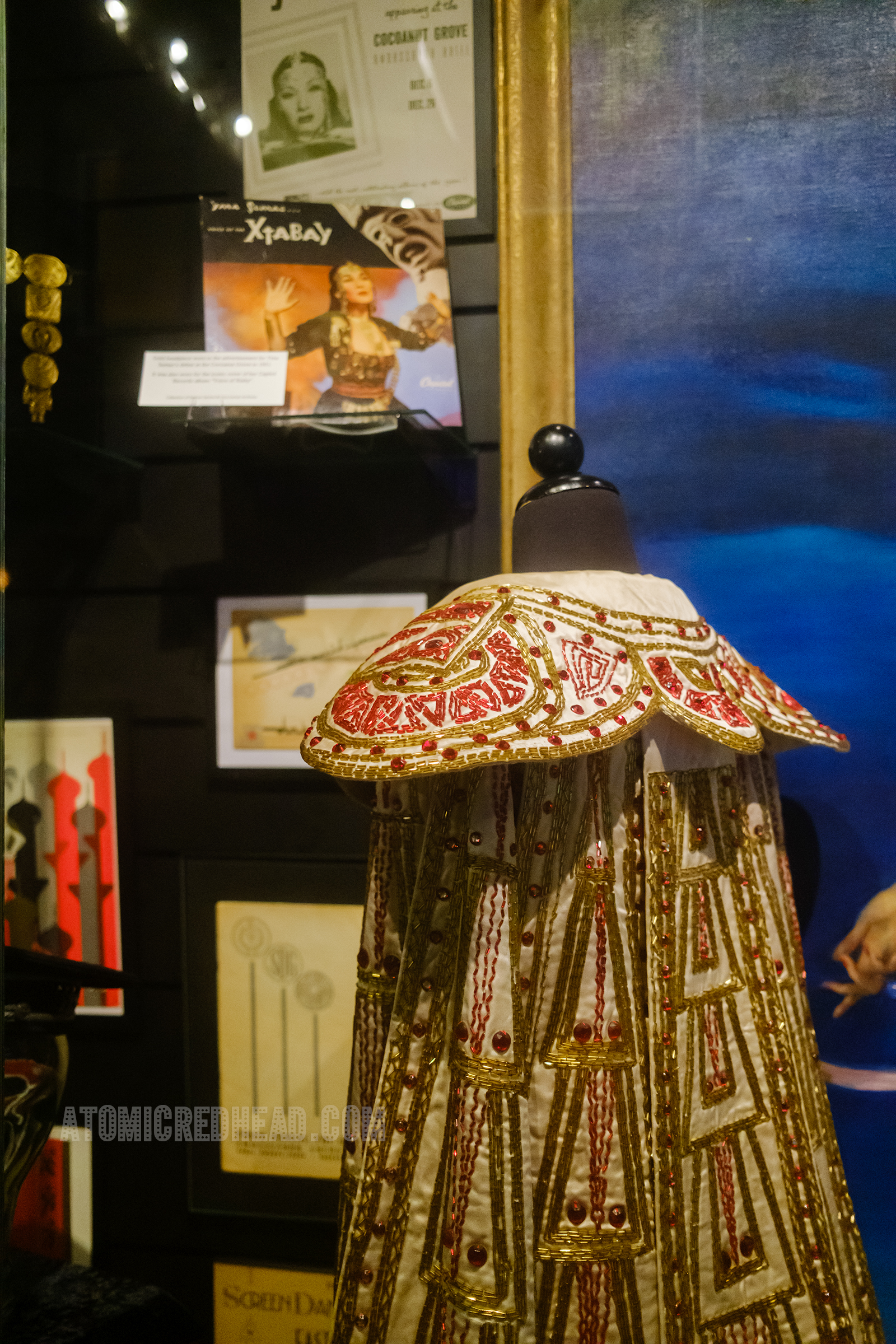 Close-up of a beaded cape in white satin with red and gold beads.