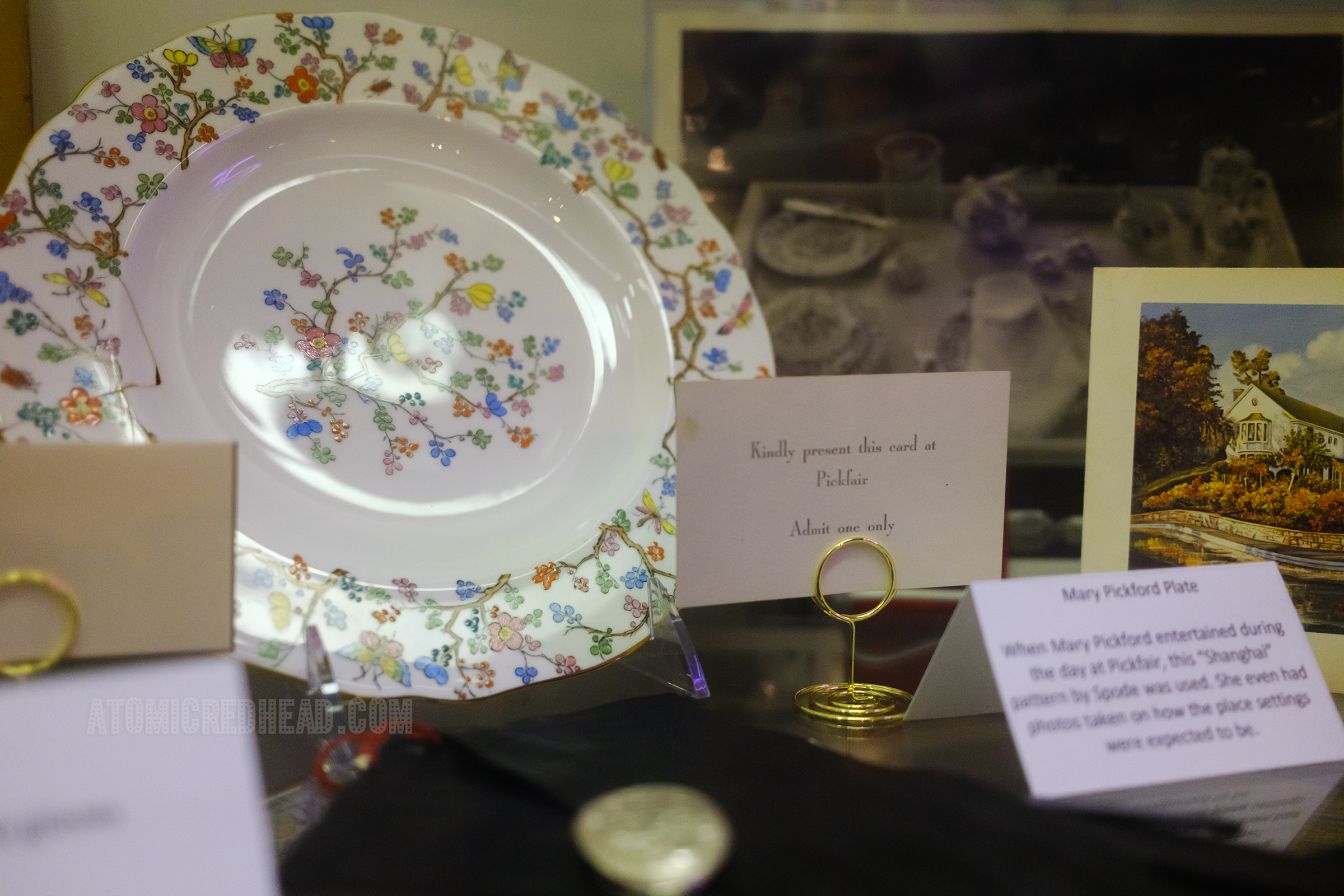 A white plate with a colorful floral pattern, next to it a small card that reads "Kindly present this card at Pickfair Admit one only"