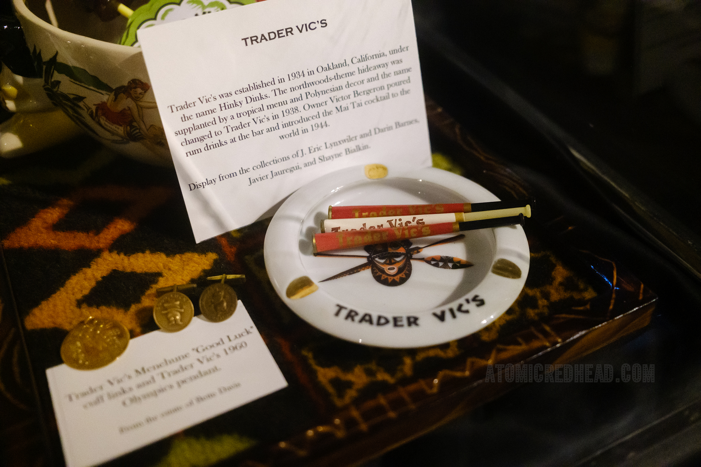 Ashtray with a large tiki mask and spears, along with cigarette holders, both reading "Trader Vic's" on them.