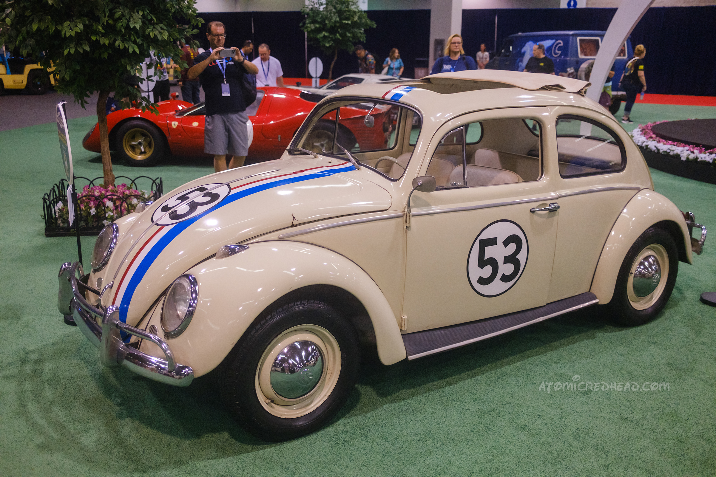 A 1963 Volkswagen Bettle, painted cream with red, white, and blue racing stripes over the hood, roof, and back. Painted on the hood and side is the number 52 inside a circle.