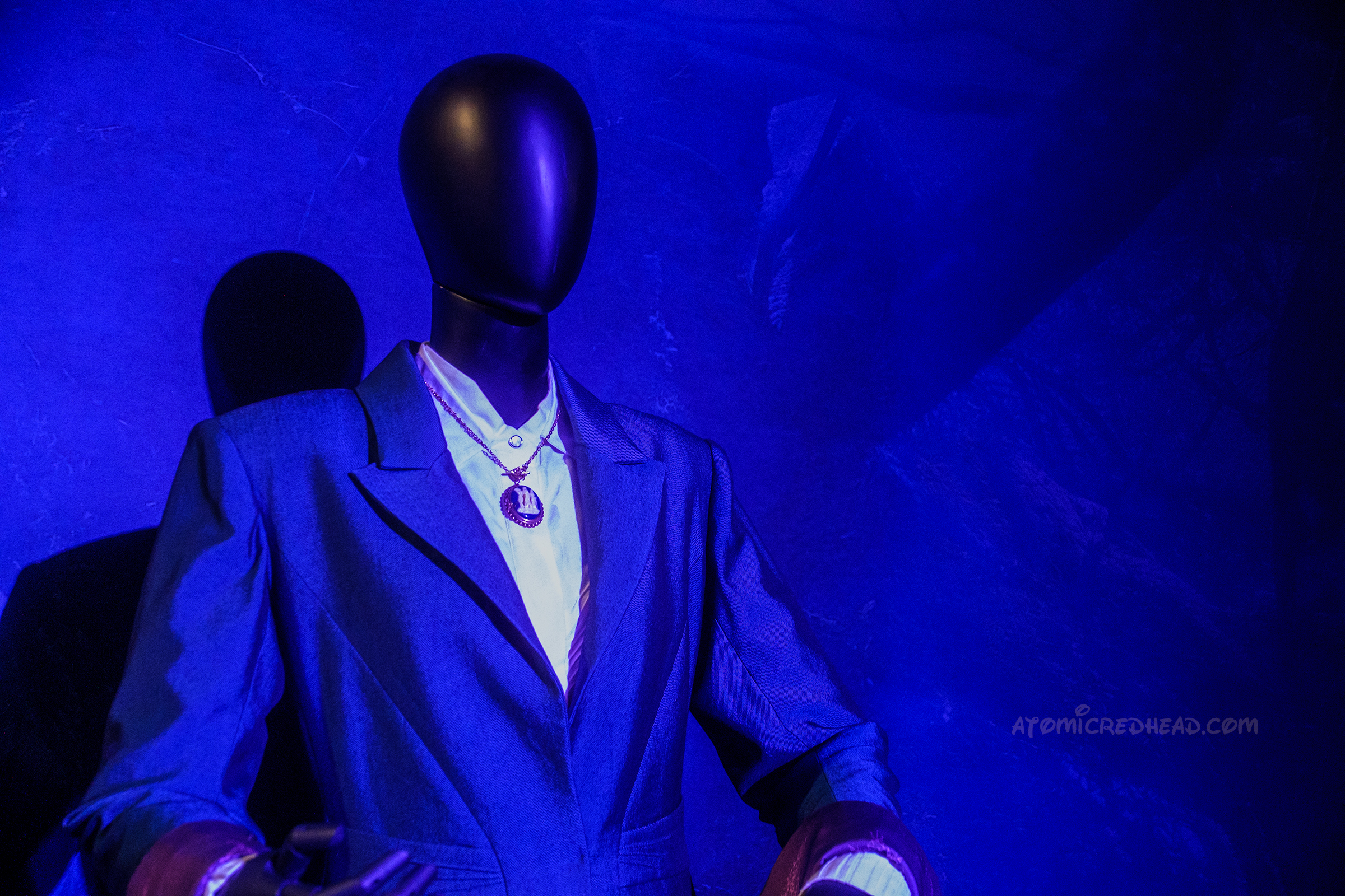 A black suit and white shirt with a cameo necklace, as worth by Agatha sits on a mannequin. 