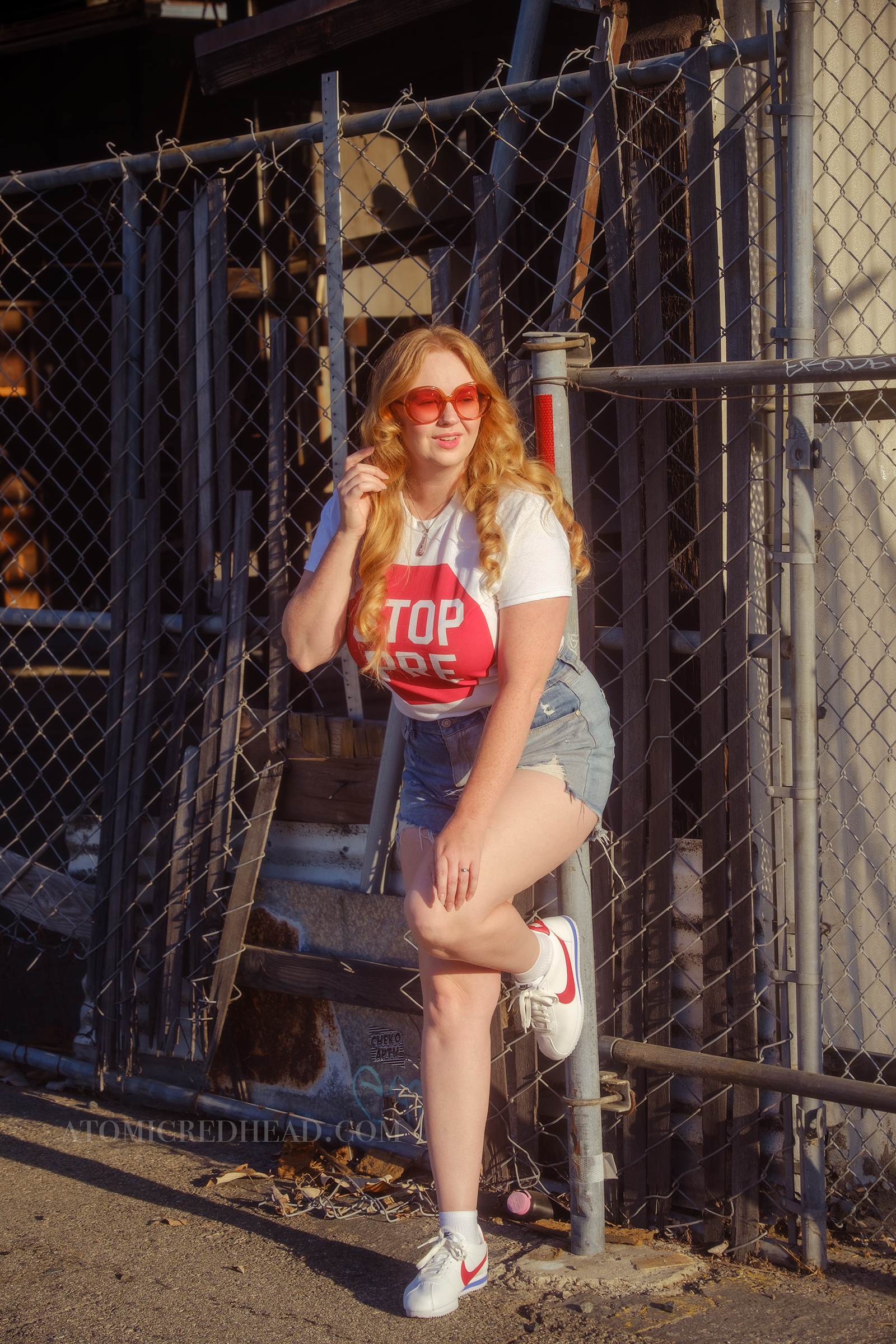 Myself, with my hair down, wearing a white tshirt featuring a red stop sign reading "Stop Pre" blue jean cut off shirts, and red, white, and blue Nike shoes.