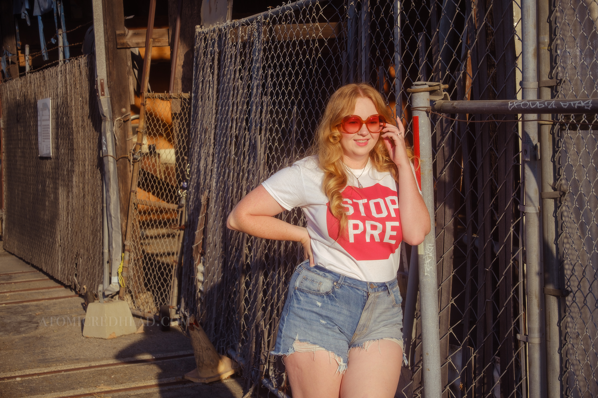 Myself, with my hair down, wearing a white tshirt featuring a red stop sign reading "Stop Pre" blue jean cut off shirts, and red, white, and blue Nike shoes.