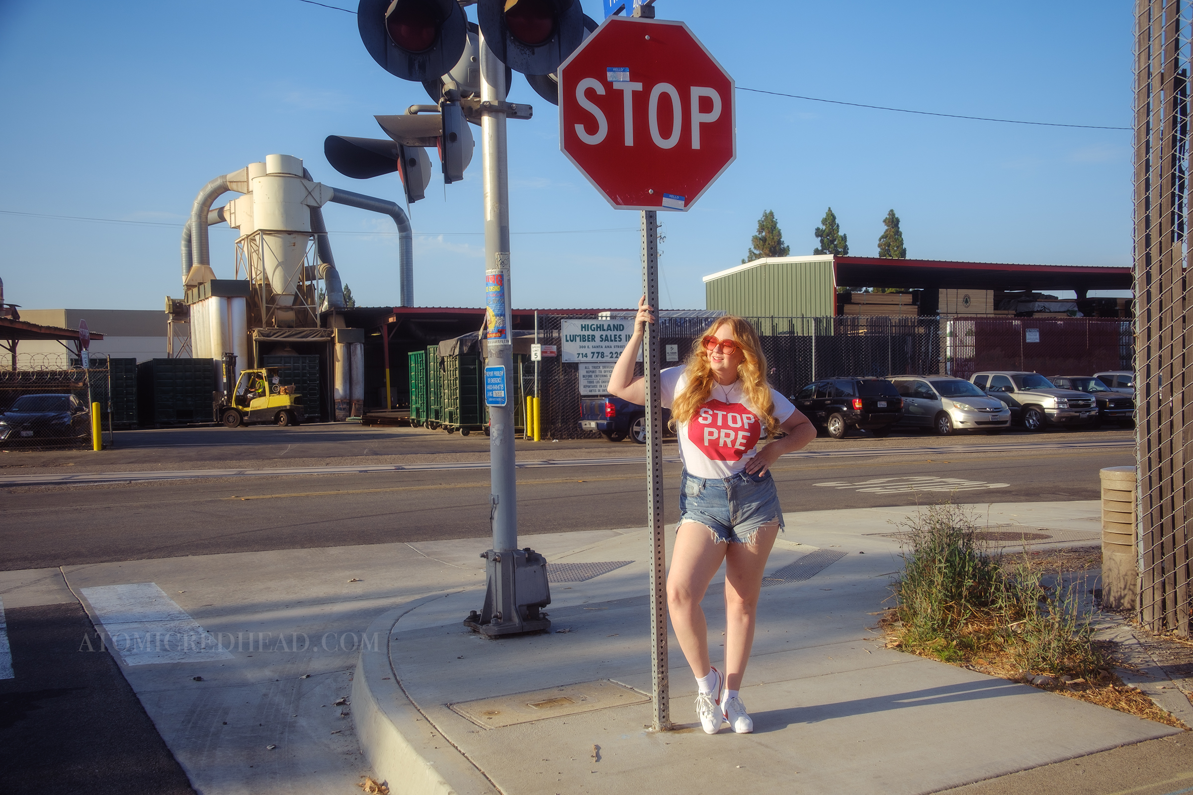 Myself, with my hair down, wearing a white tshirt featuring a red stop sign reading "Stop Pre" blue jean cut off shirts, and red, white, and blue Nike shoes.
