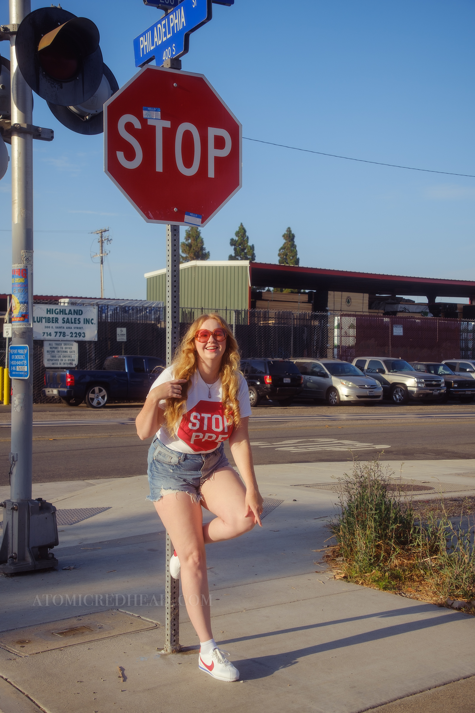 Myself, with my hair down, wearing a white tshirt featuring a red stop sign reading "Stop Pre" blue jean cut off shirts, and red, white, and blue Nike shoes.