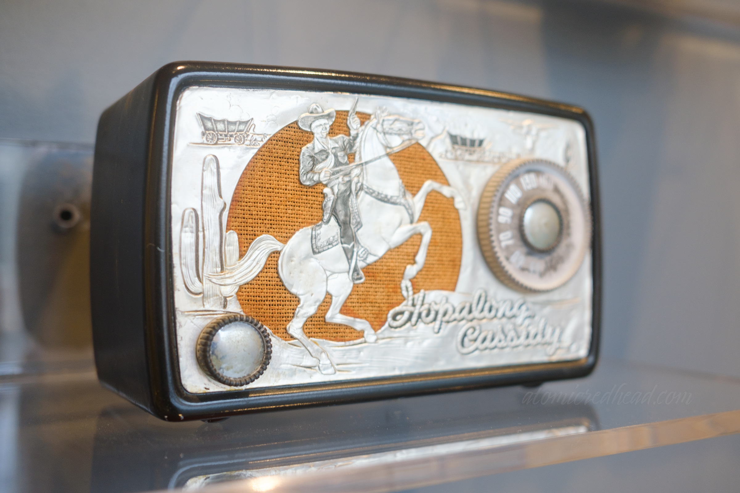 A black radio with a silver front features a cowboy on a horse, script in the corner reads "Hopalong Cassidy"
