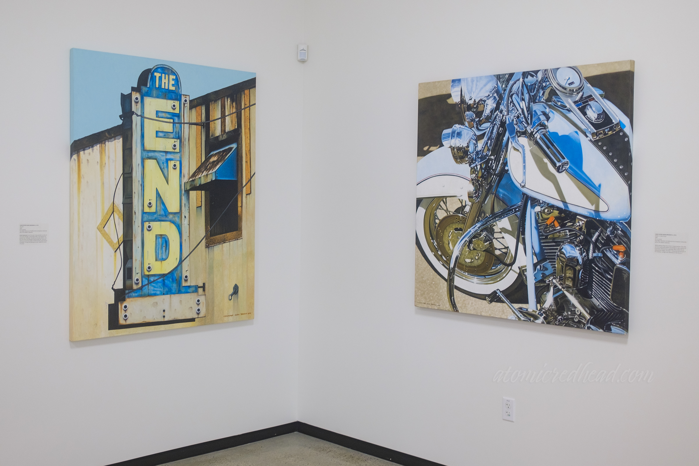 Two realistic paintings, on of a faded neon sign reading "The End" another of a motorcycle.
