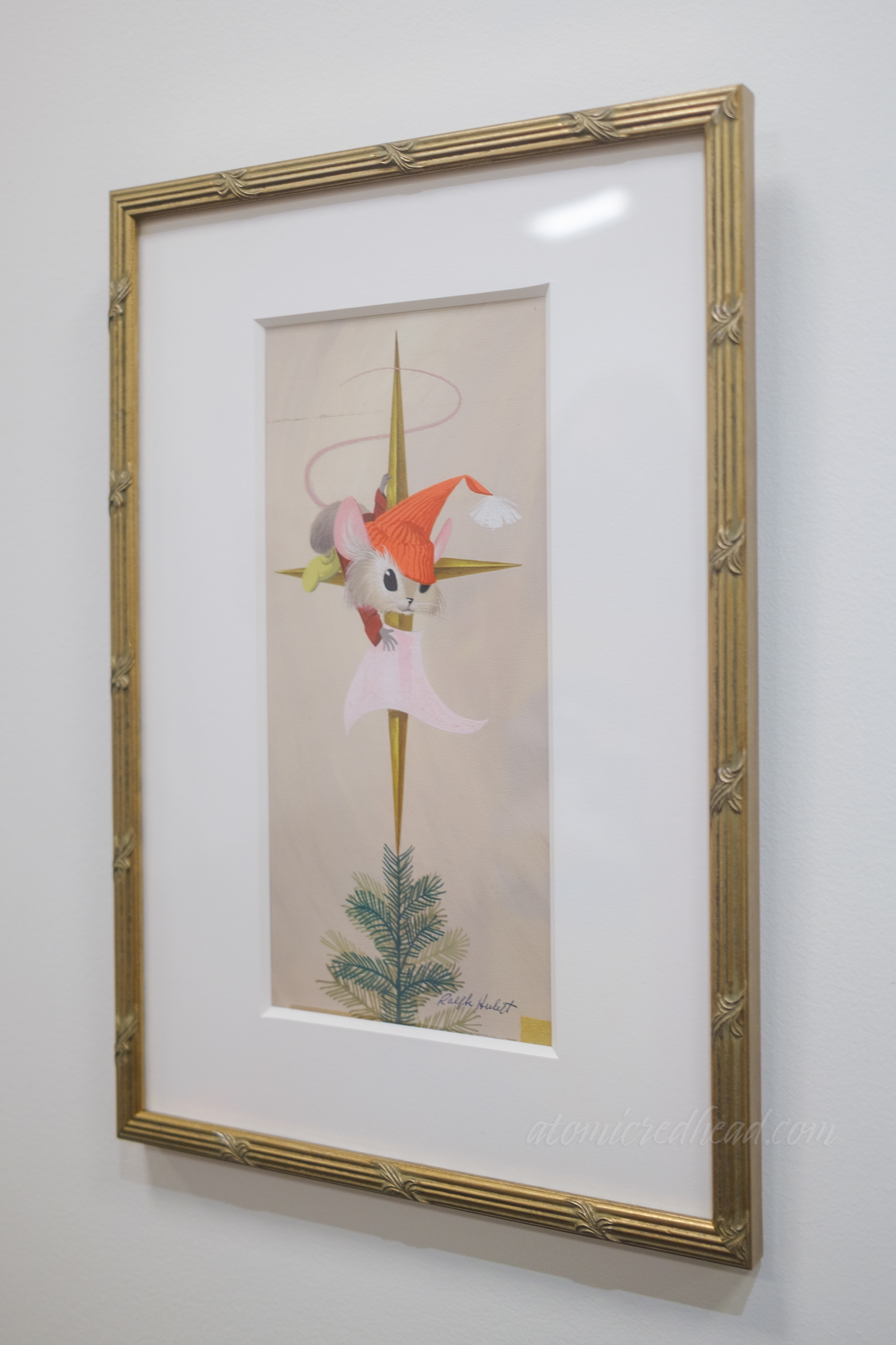 A small mouse wearing a Santa hat shines a star atop a Christmas tree.