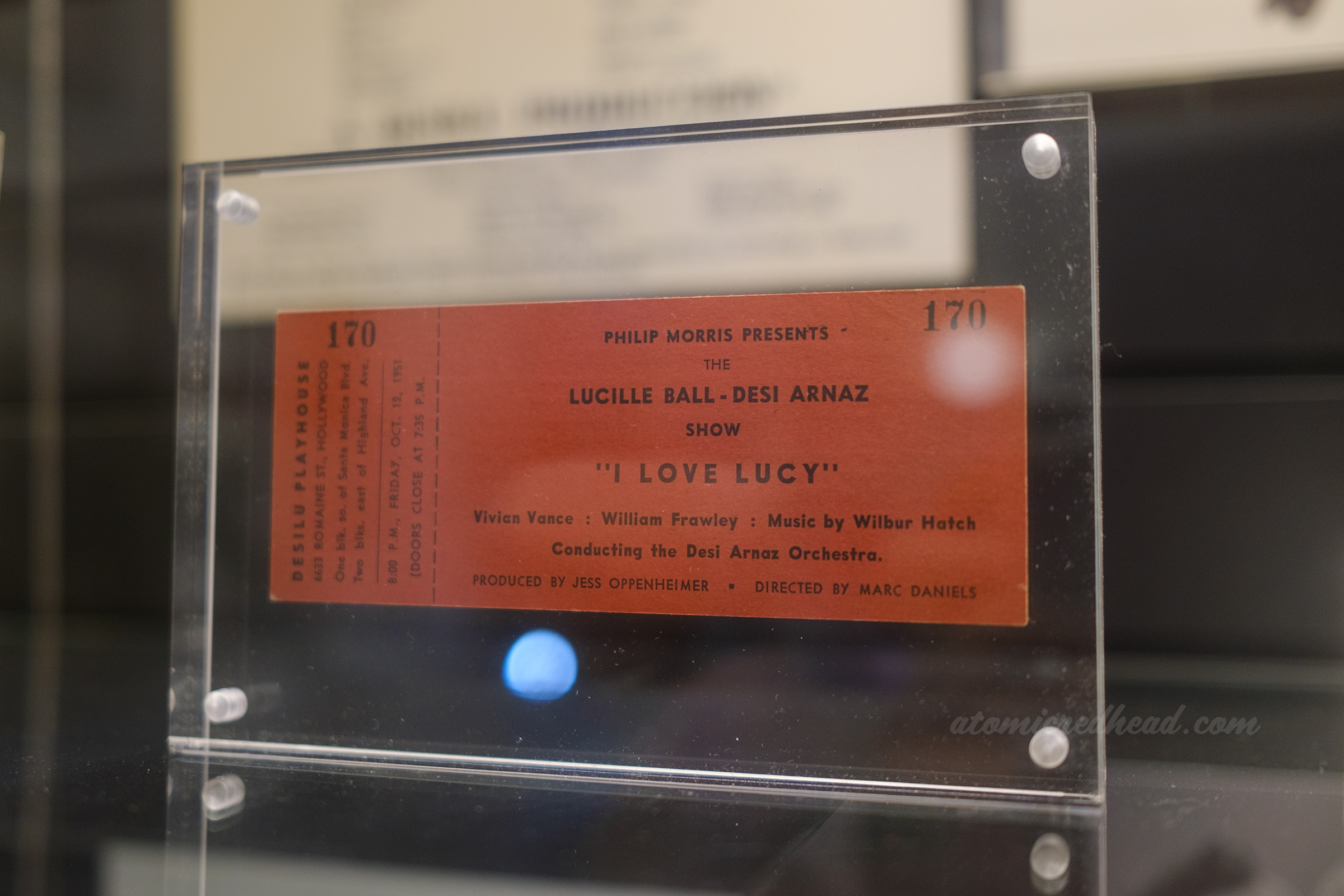 A red ticket to an episode of I Love Lucy which reads'Philip Morris Presents the Lucille Ball - Desi Arnaz Show 'I Love Lucy' Vivian Vance : William Frawley : Music by Wilbur Hatch Conducting the Desi Arnaz Orchestra Produced by Jess Oppenheimer Directed by Marc Daniels.