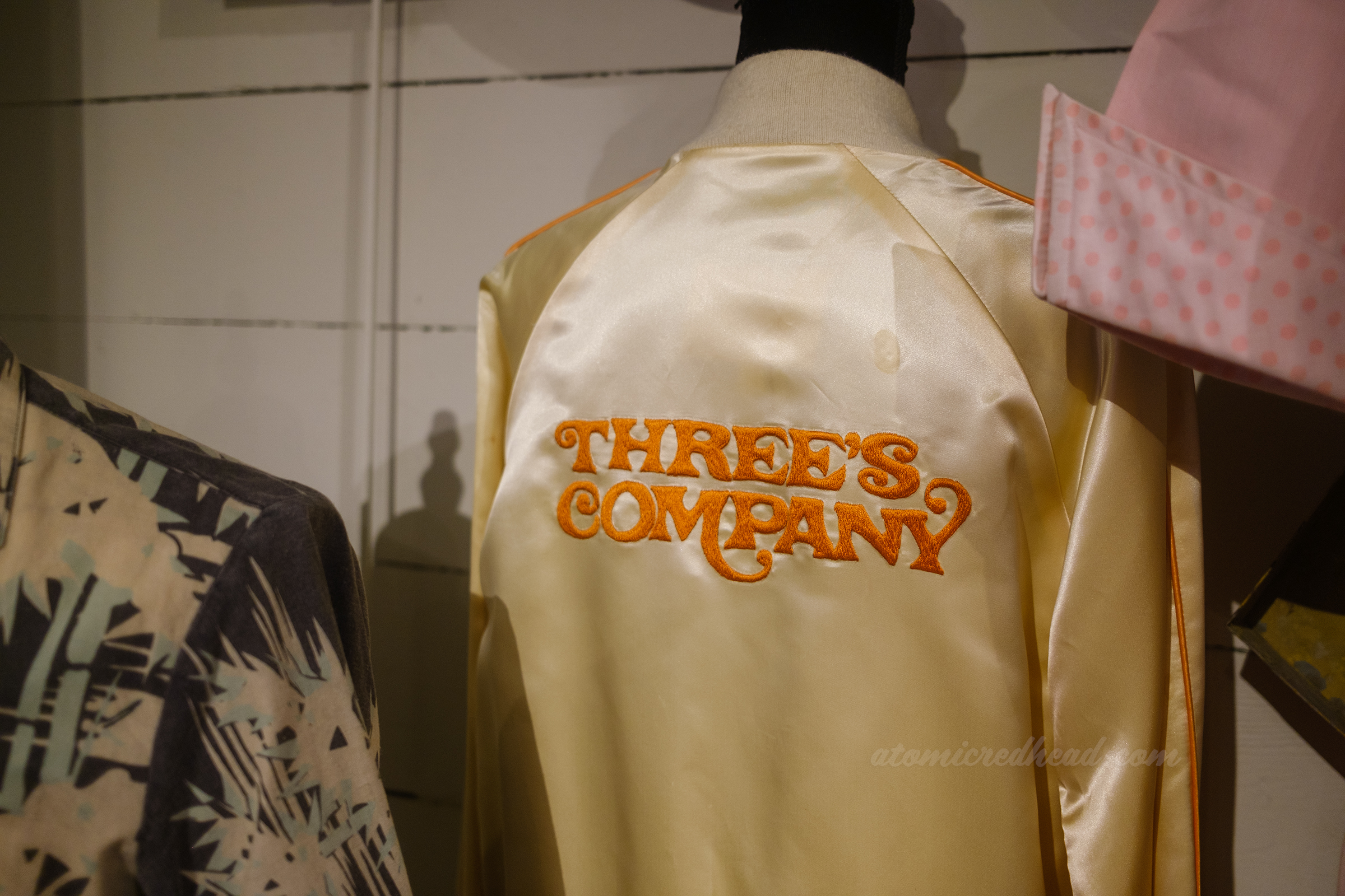 A white satin jacket with "Three's Company" embroidered on the back.