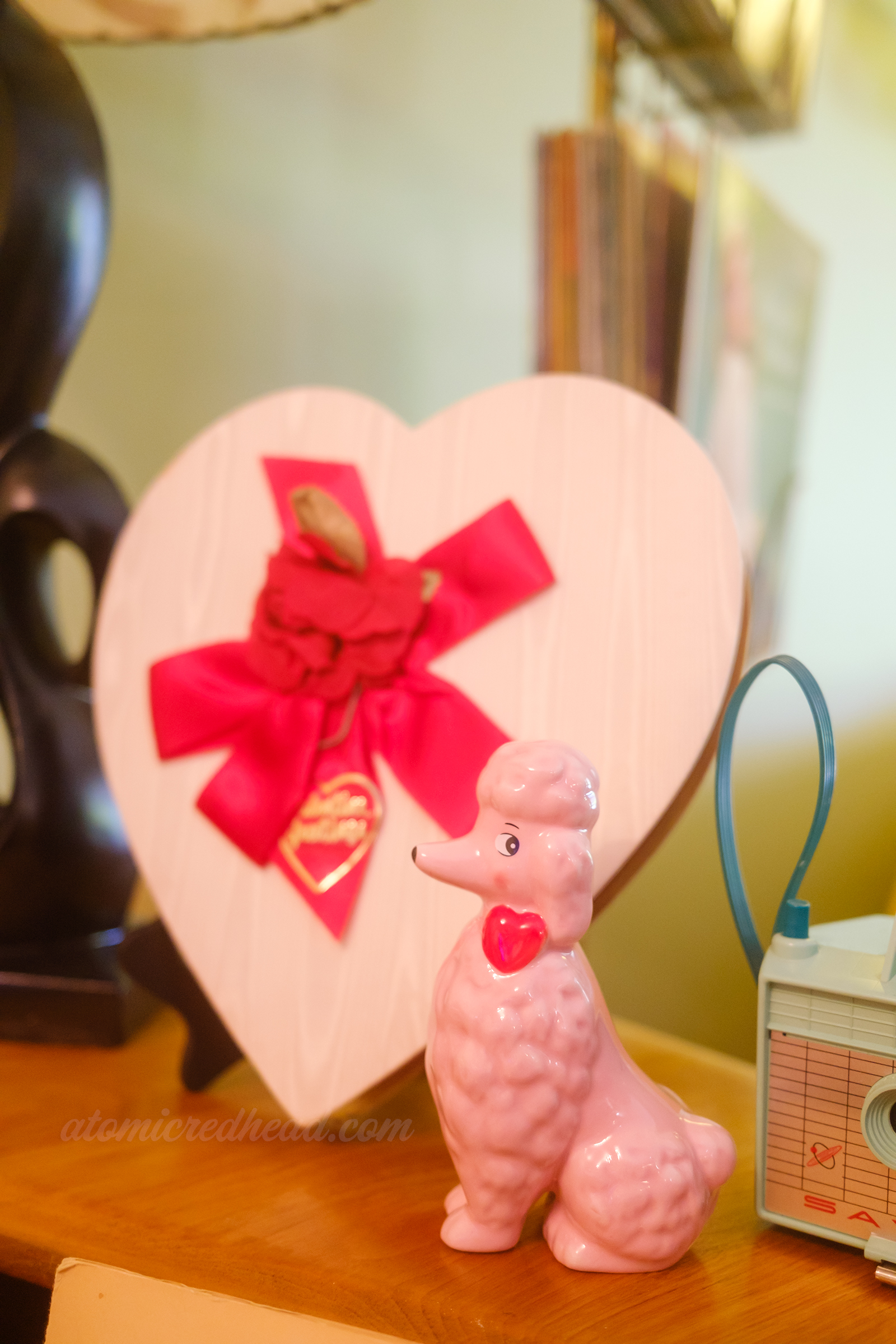 Close-up of a white with red bow heart shaped chocolate box and a pink poodle.