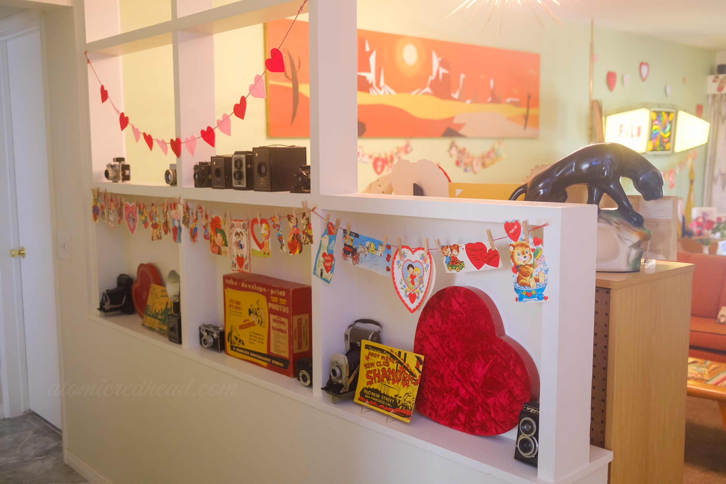 View of our built in room divider that separates the hallway from the living room, various vintage valentines hang from it along with heart shaped chocolate boxes inside.