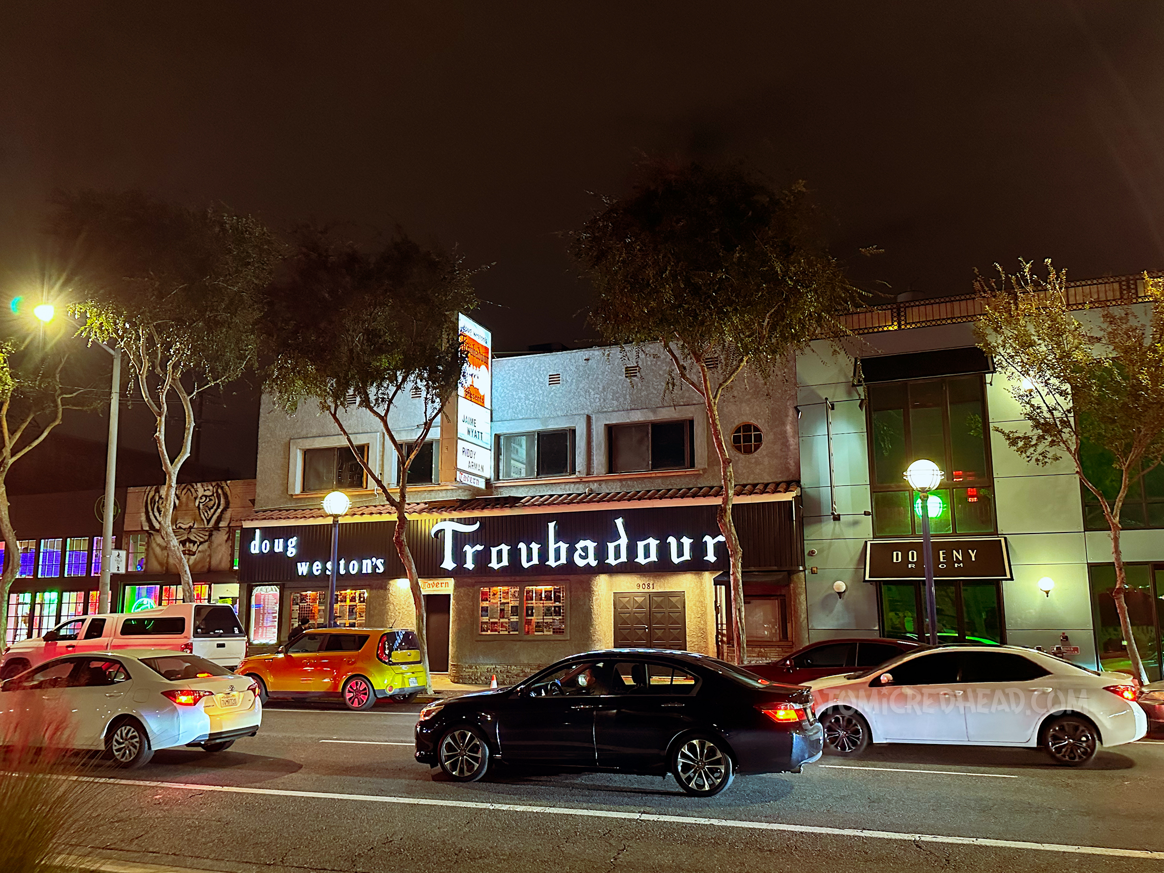 Exterior of The Troubadour at night, a lighted sign in old English script reads The Troubadour across the top.