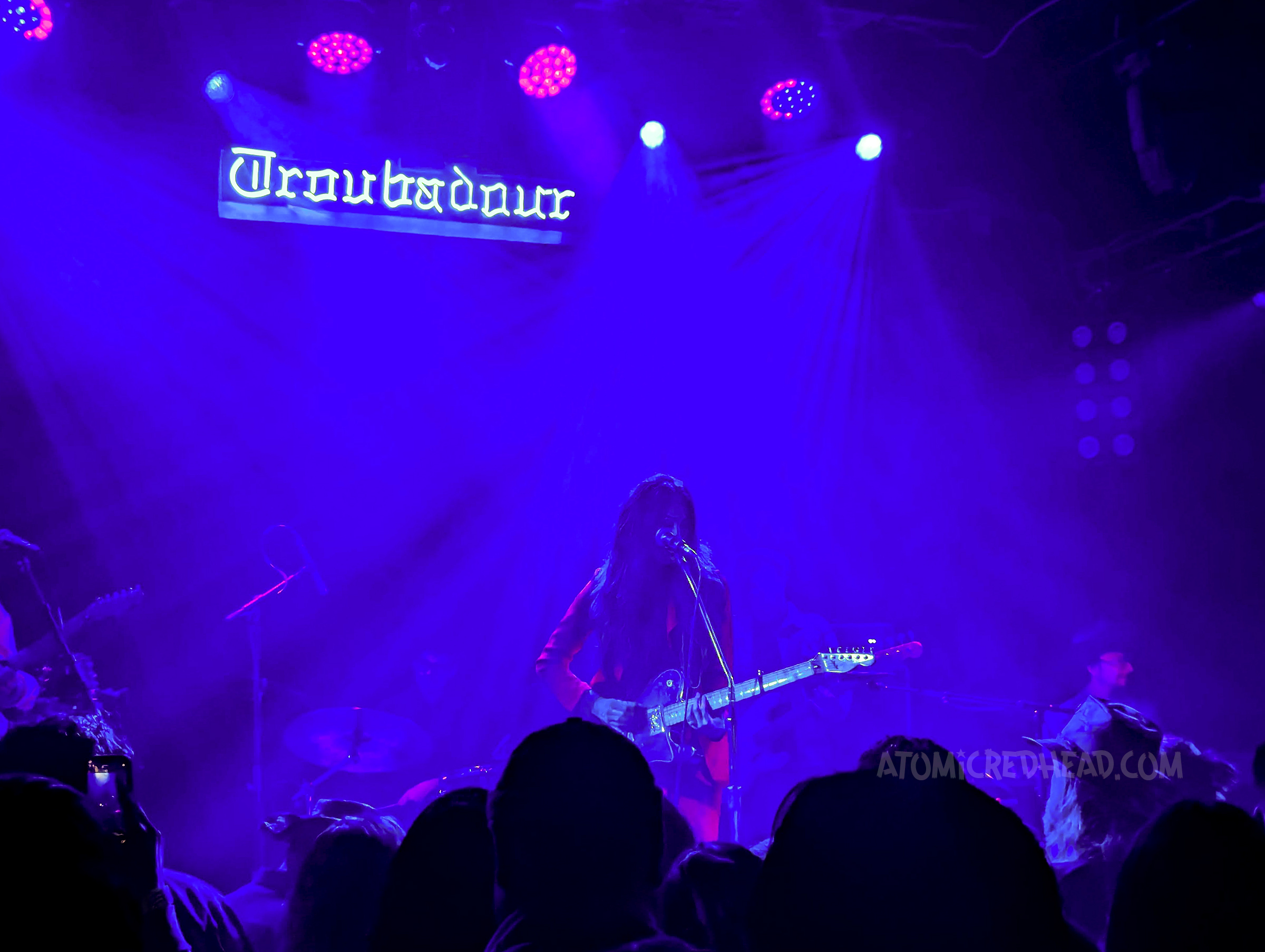 Interior, under blue lights Jaime Wyatt performs, a neon sign reading "Troubadour" is above her.