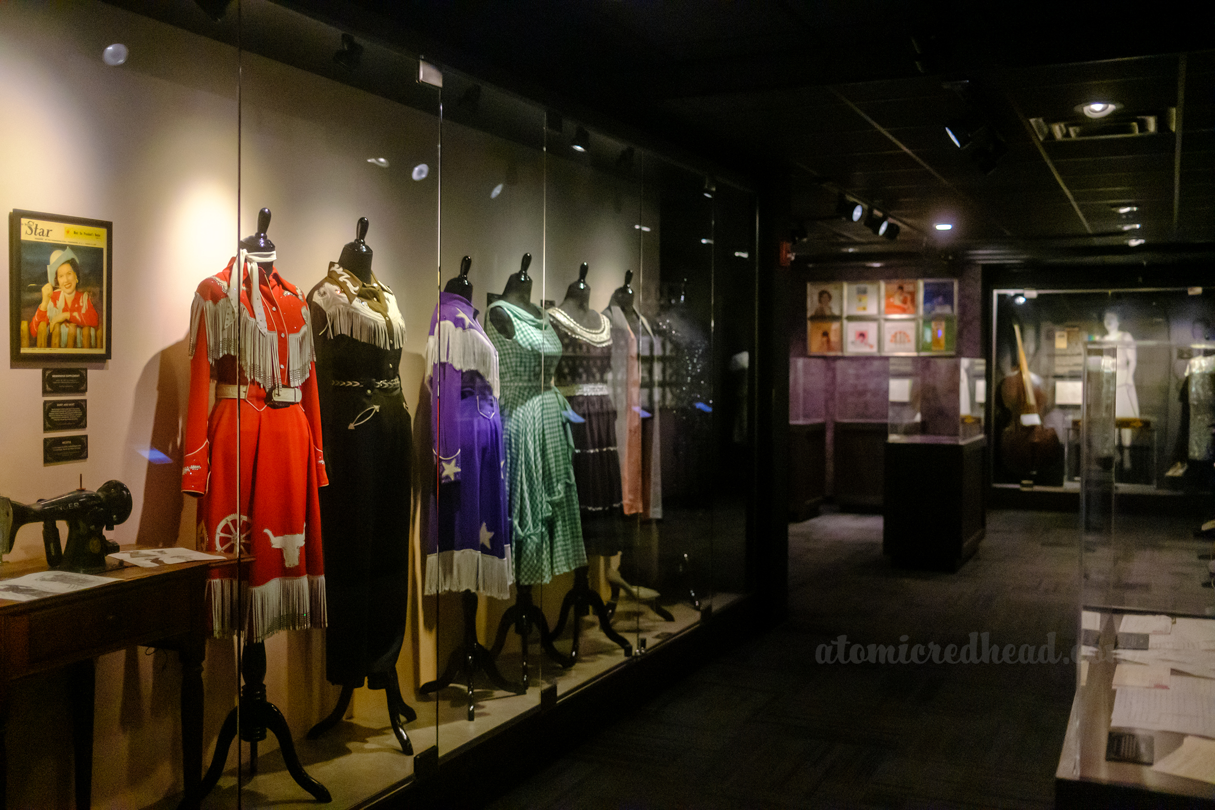 A collection of stage costumes worn by Patsy Cline on mannequins on display behind glass.