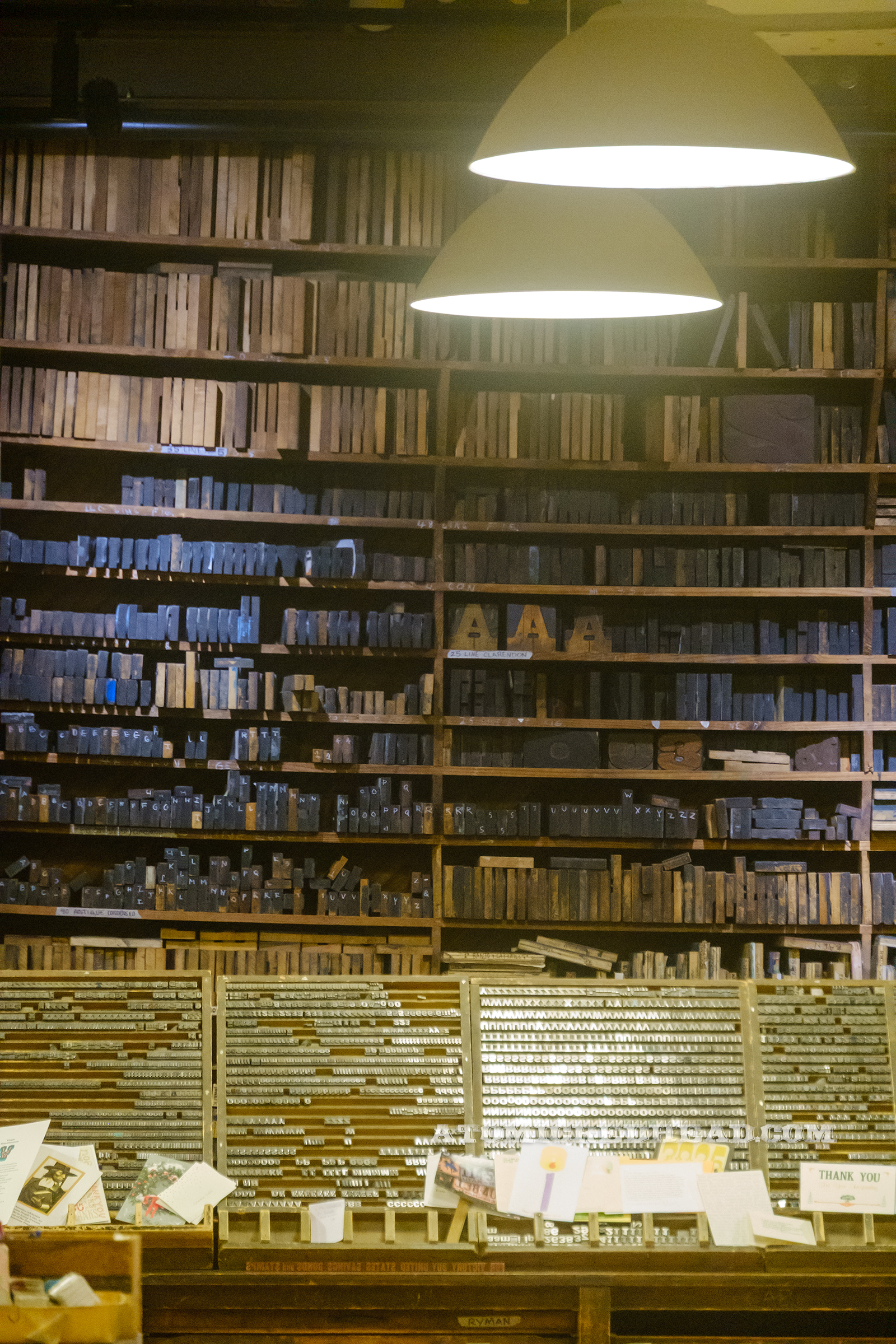 A portion of the back wall, floor to ceiling shelving with printing blocks stacked, so heavy they cause the shelving to bow.