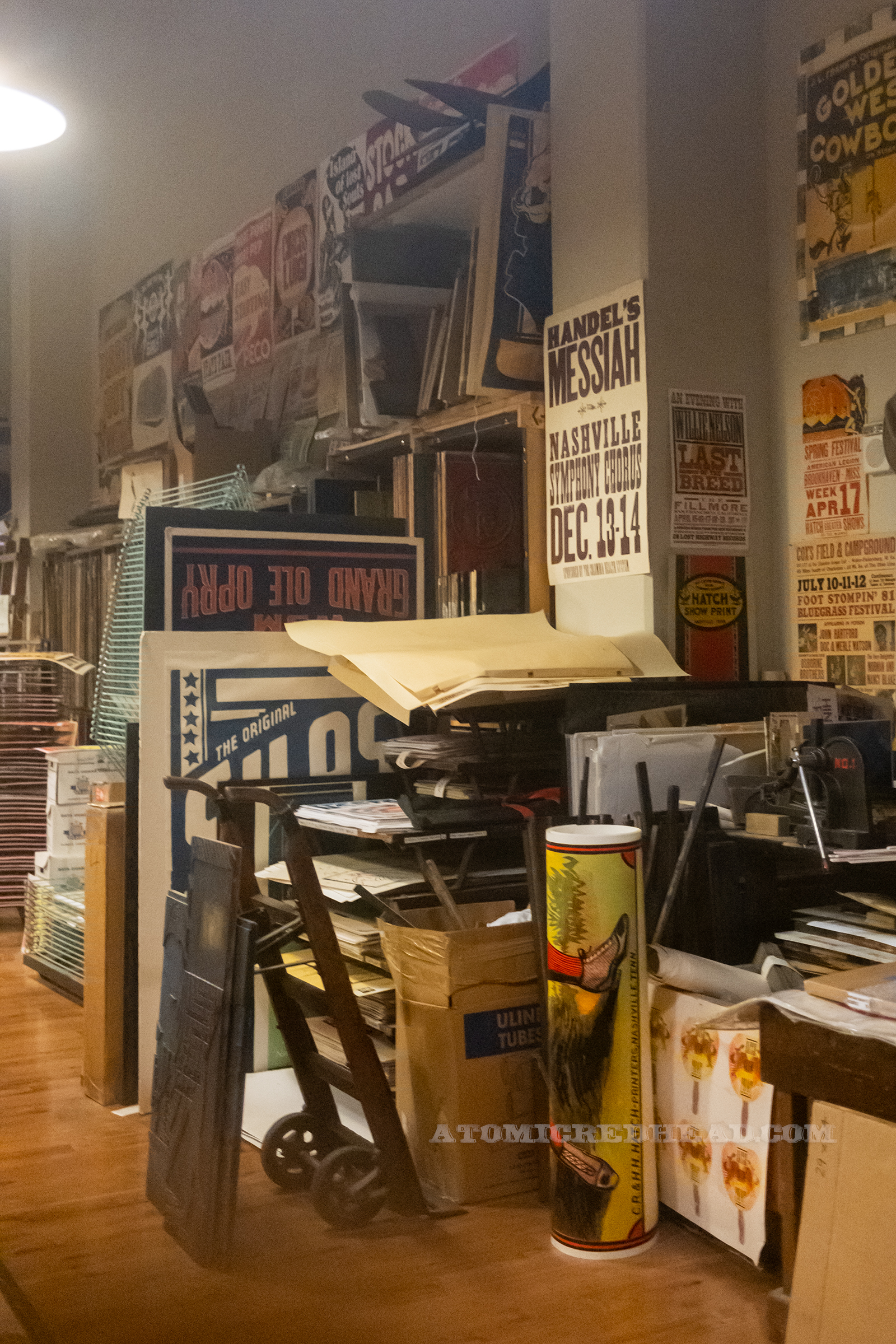 A corner of the shop with shelves and a desk scattered with prints.